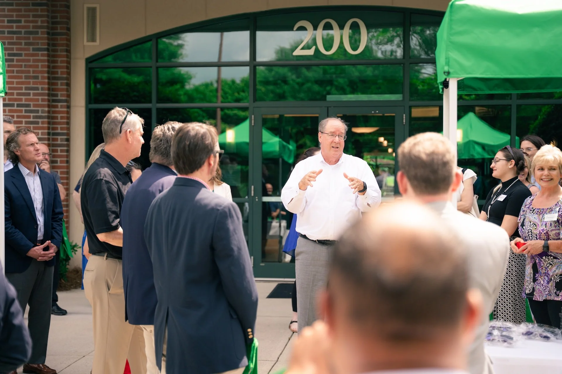Man in white shirt speaking to a group of people outside a building with the number 200 on the door.