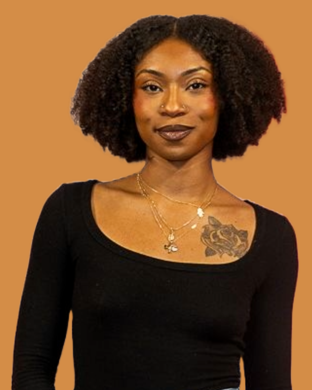 Portrait of a woman with natural curly hair, wearing a black top and layered necklaces, standing against a plain brown background.