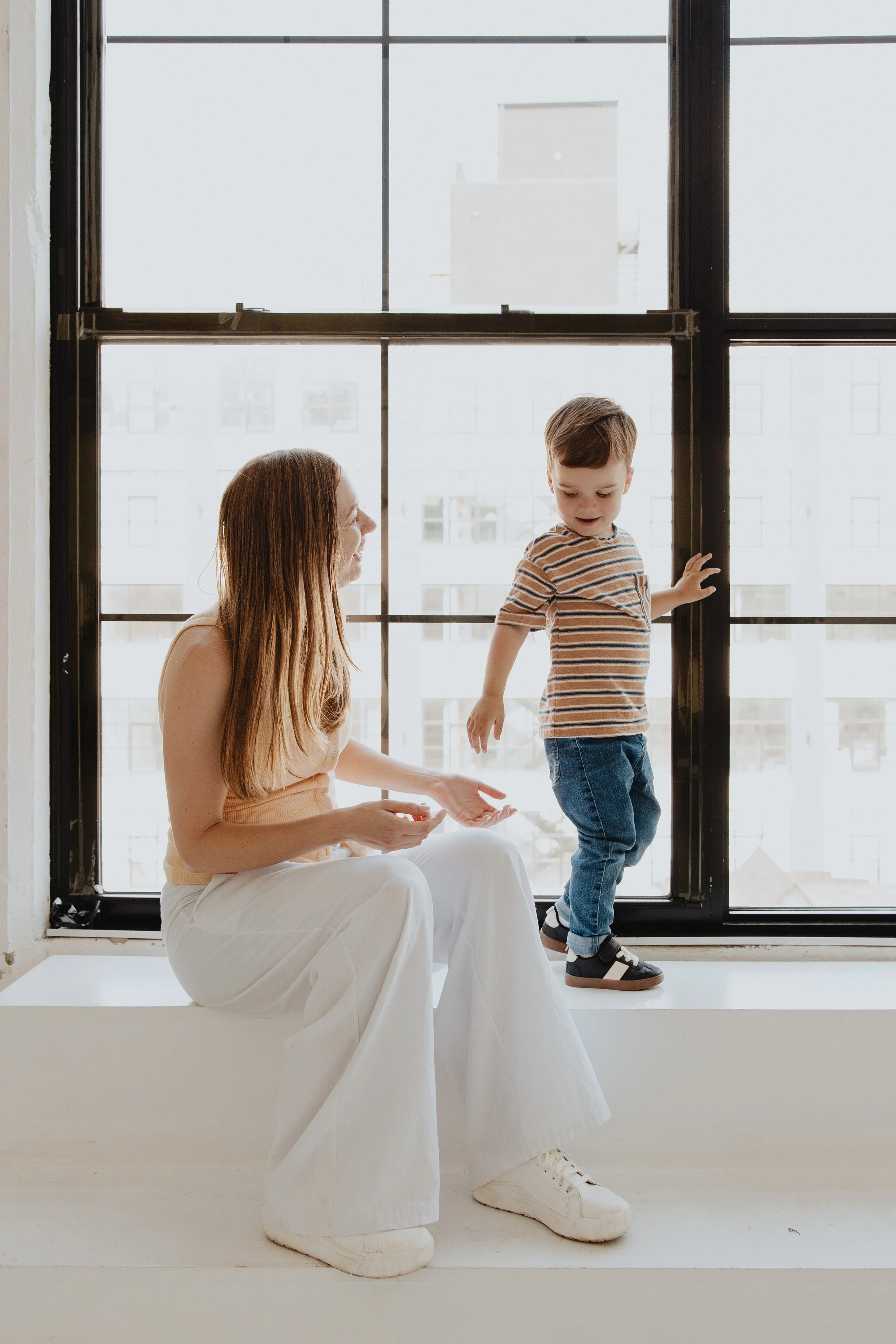 Adult and toddler sweetly interacting in front of a big window