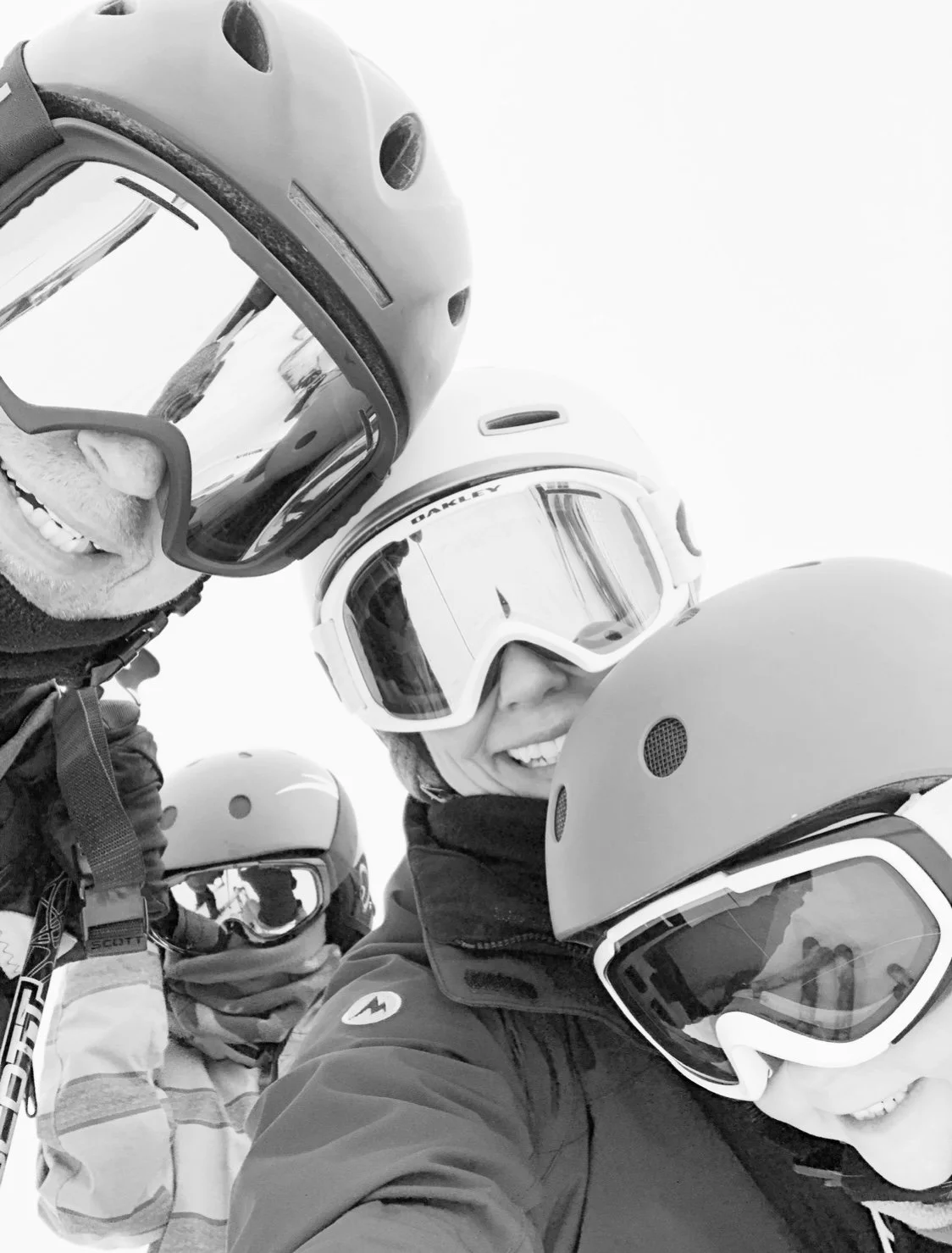 Group of people in ski gear, wearing helmets and goggles, smiling for a selfie on a snowy mountain.