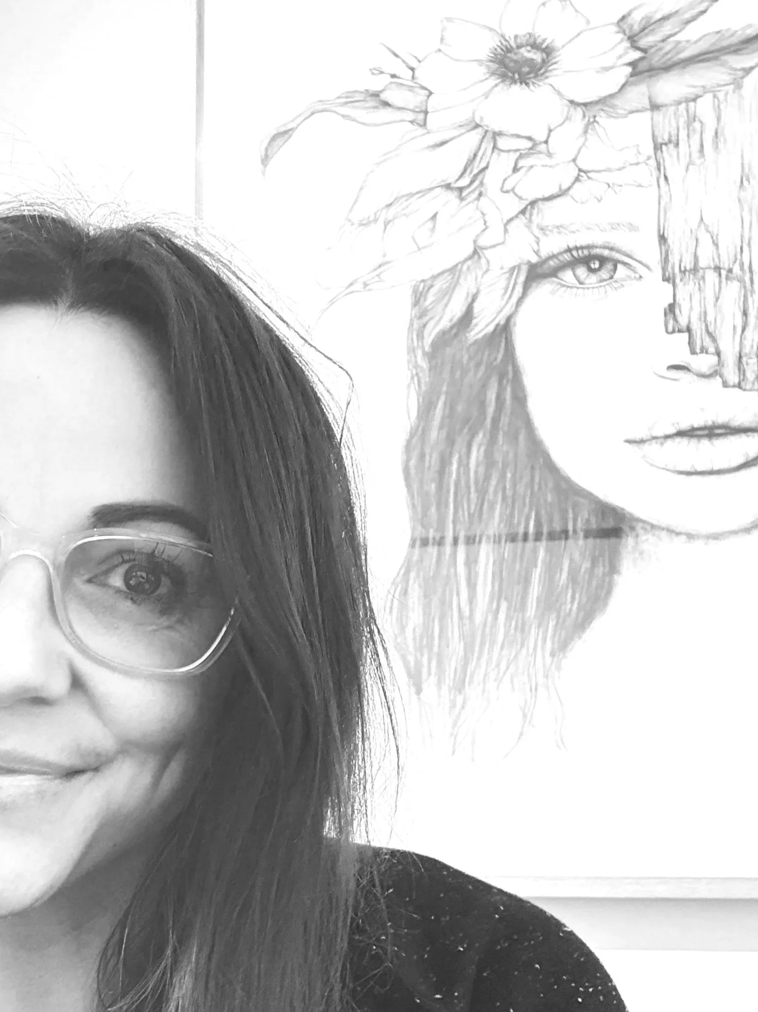 Black and white photo of a young woman with glasses showing only part of her face, with long dark hair, in front of a framed artwork of a woman's face with flowers and a tree.