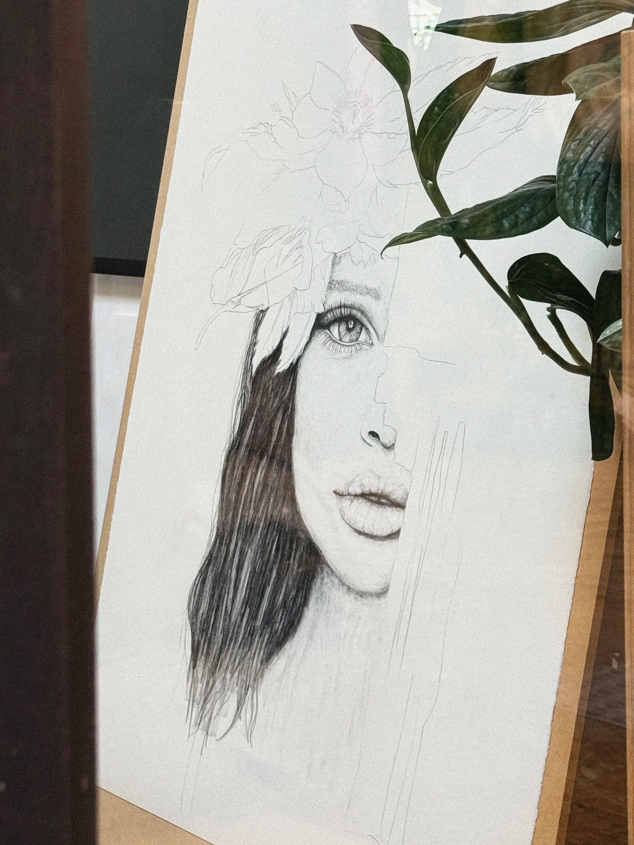 A partially completed pencil drawing of a woman's face with detailed eye, lips, and long hair, with some sketches of a flower and leaves above.