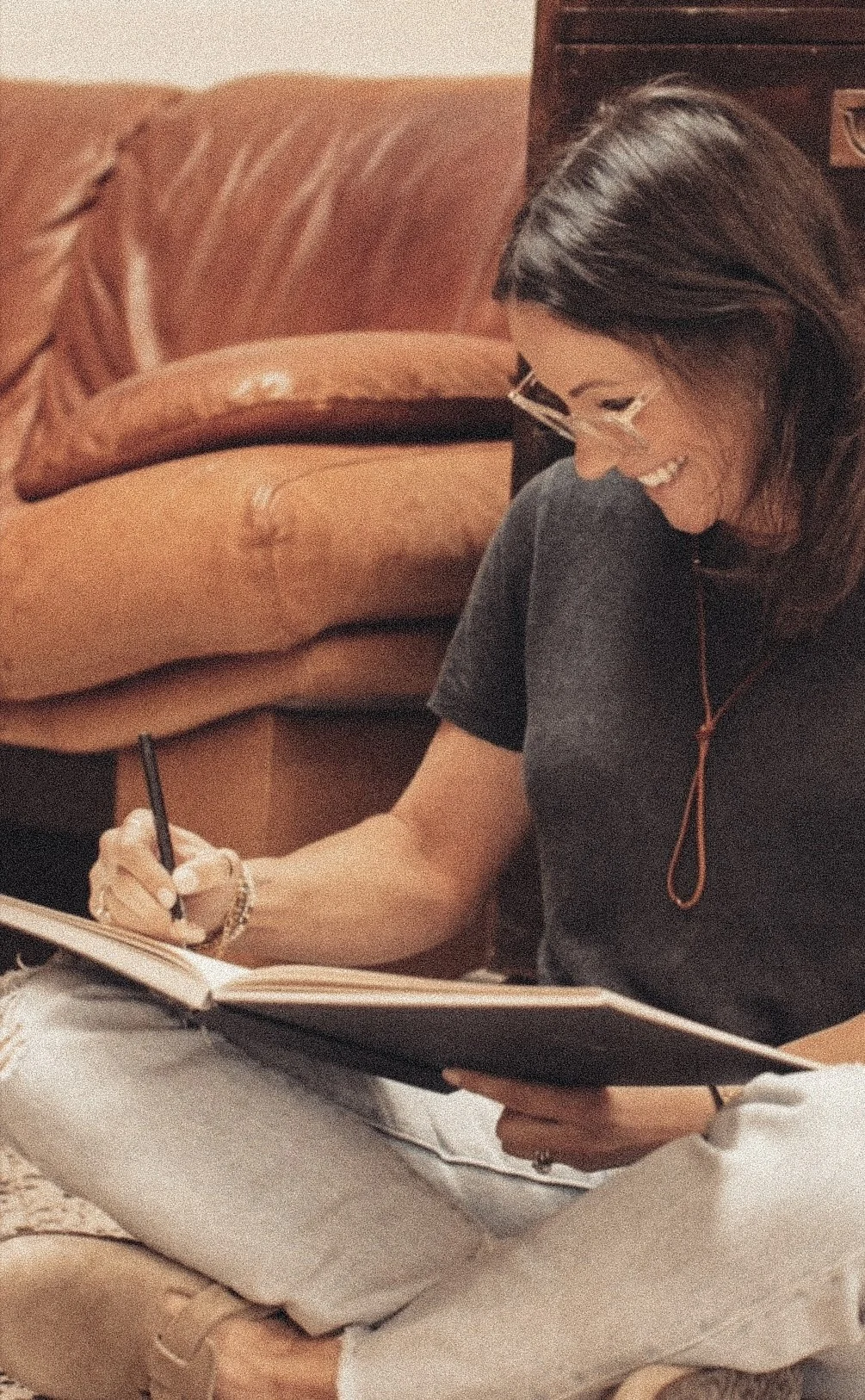 A woman sitting on the floor, smiling, writing in a notebook.