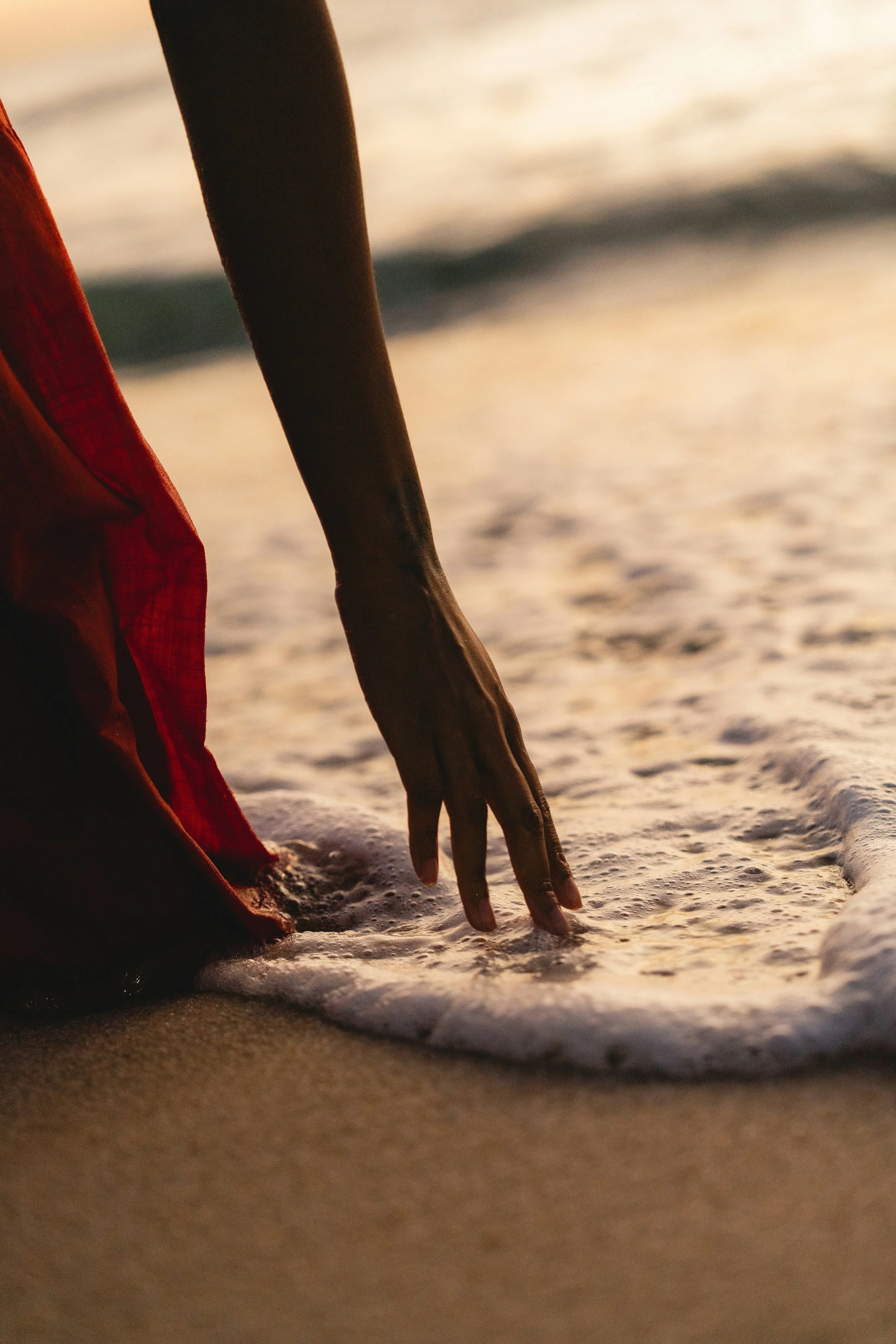 Person in red clothing touching the water at the beach during sunset.