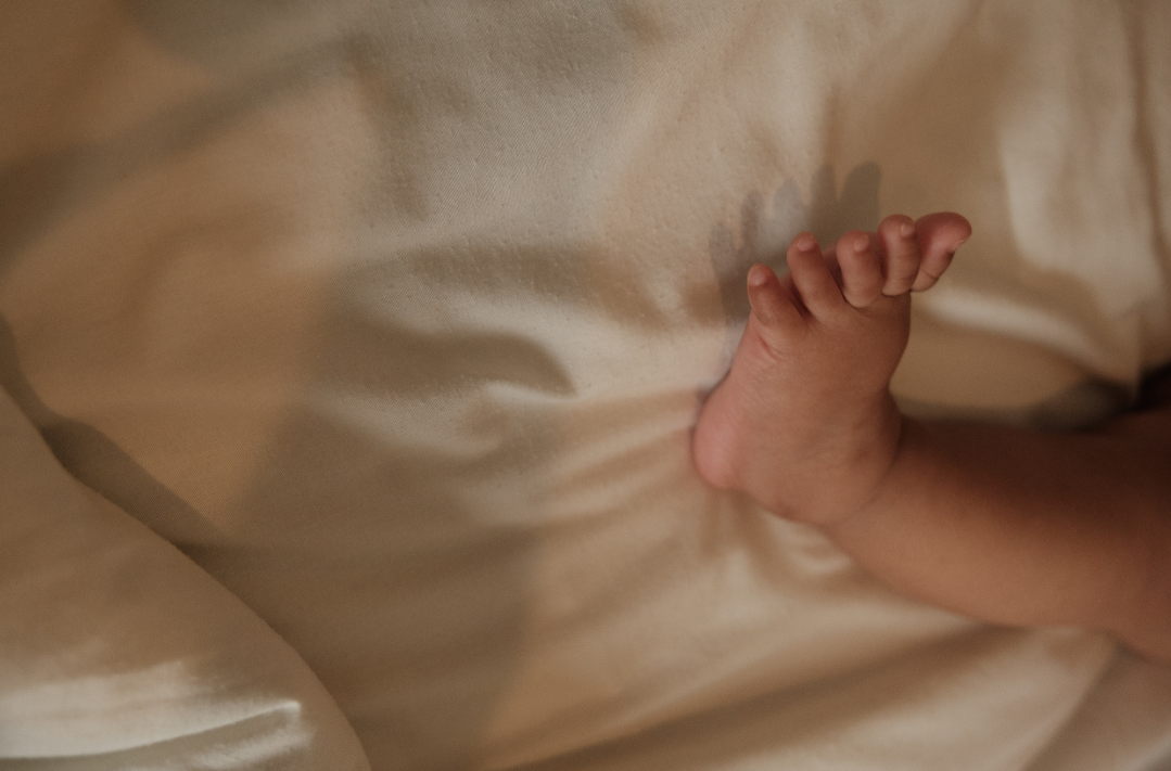 Close-up of a newborn baby's hand resting on a soft, cream-colored fabric blanket.