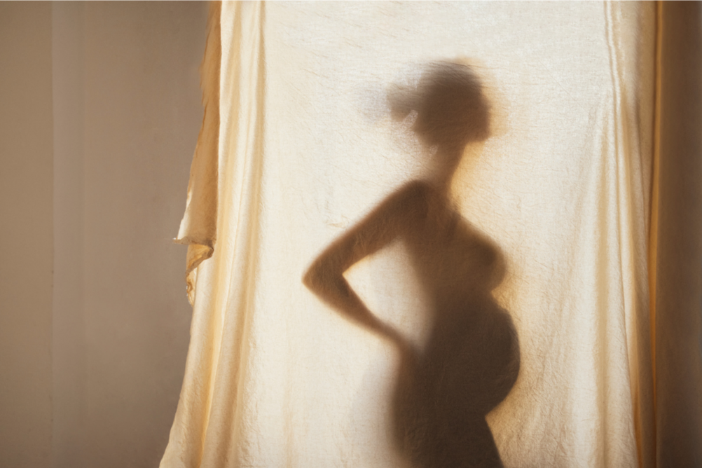 Shadow of a pregnant woman standing in front of a curtain.