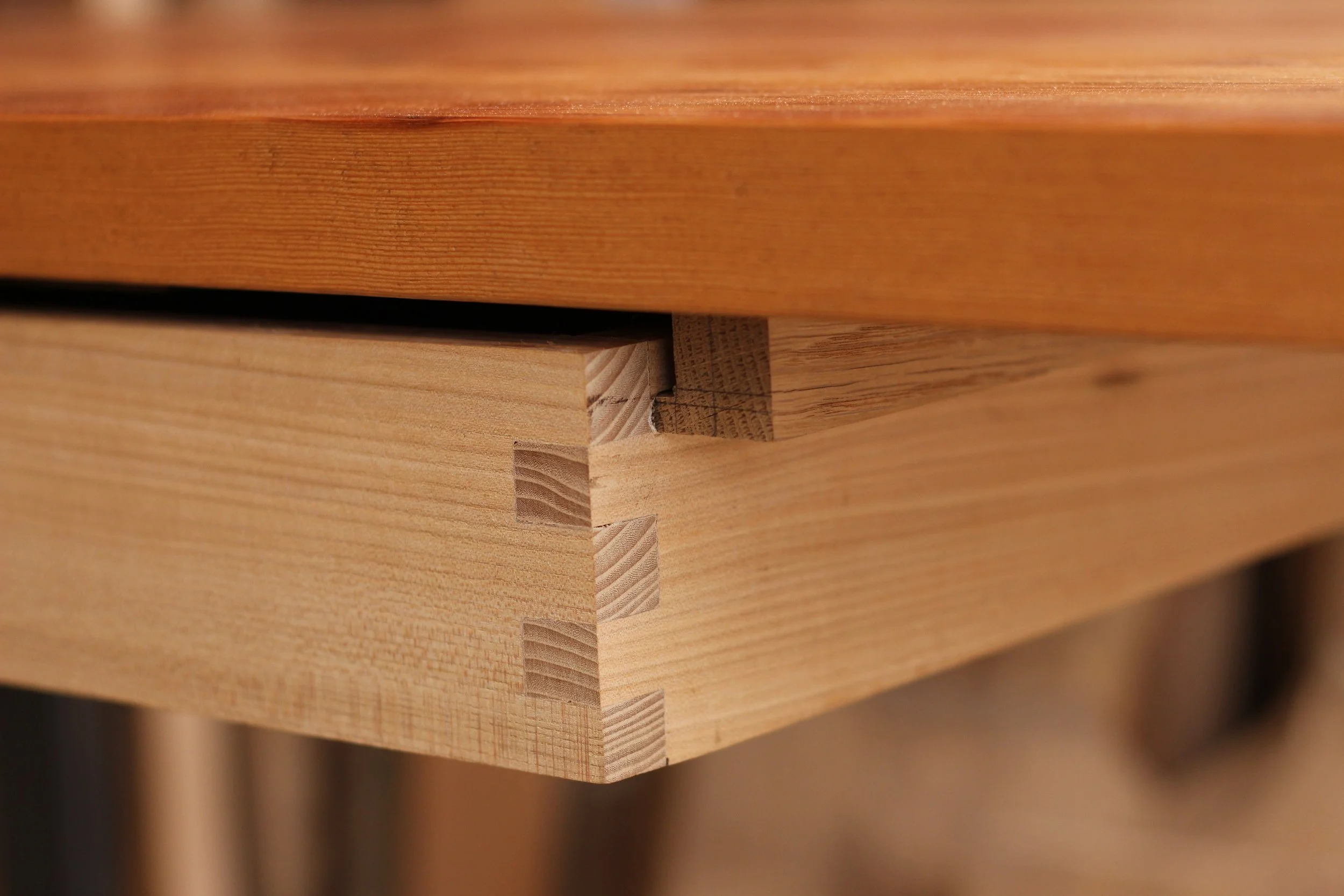 Close-up of wooden furniture corner with dovetail joint showing interlocking wood pieces.