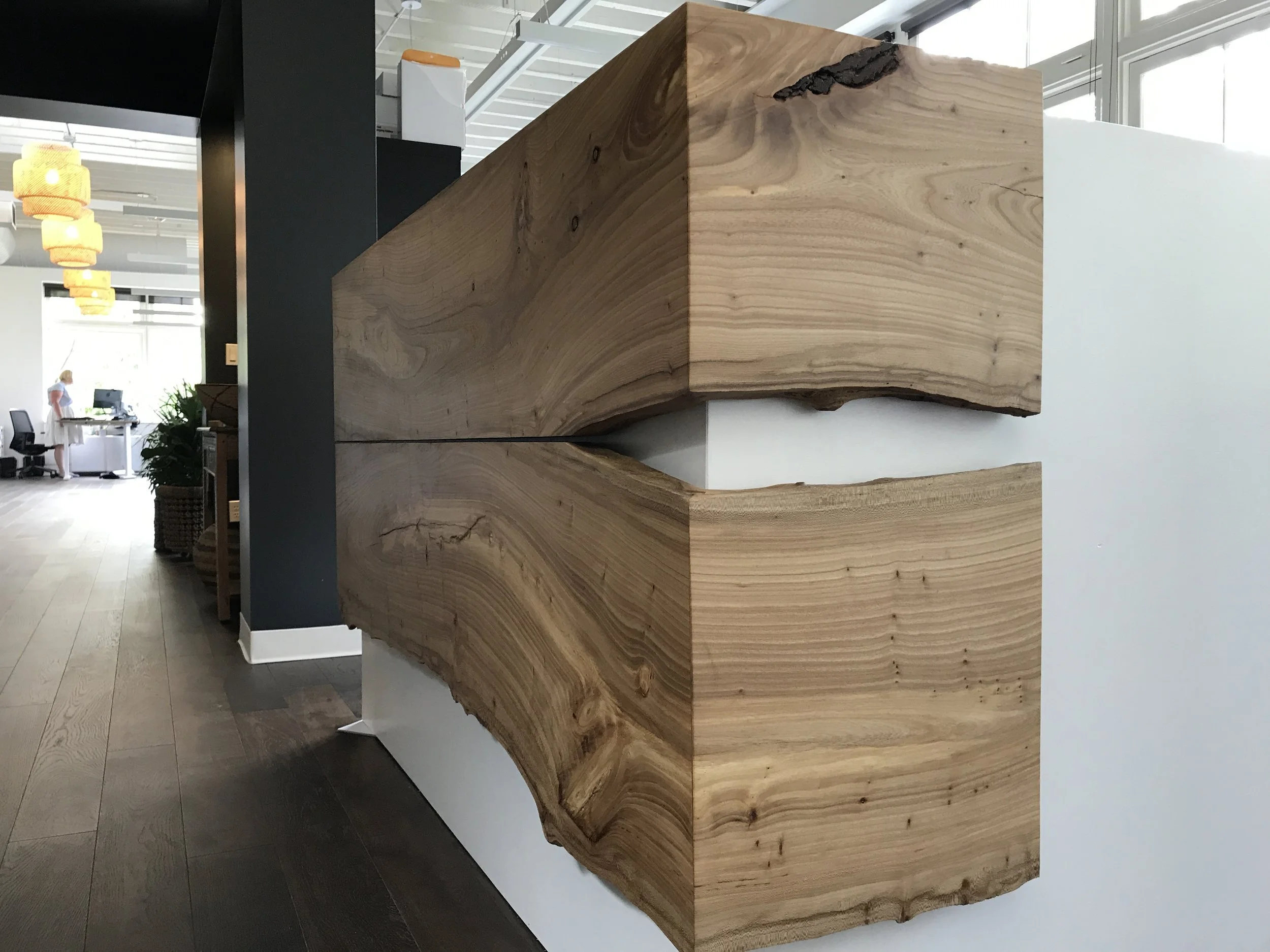 Close-up of a modern reception desk made of large, natural wooden blocks with visible grain and knots, situated in a bright office space.