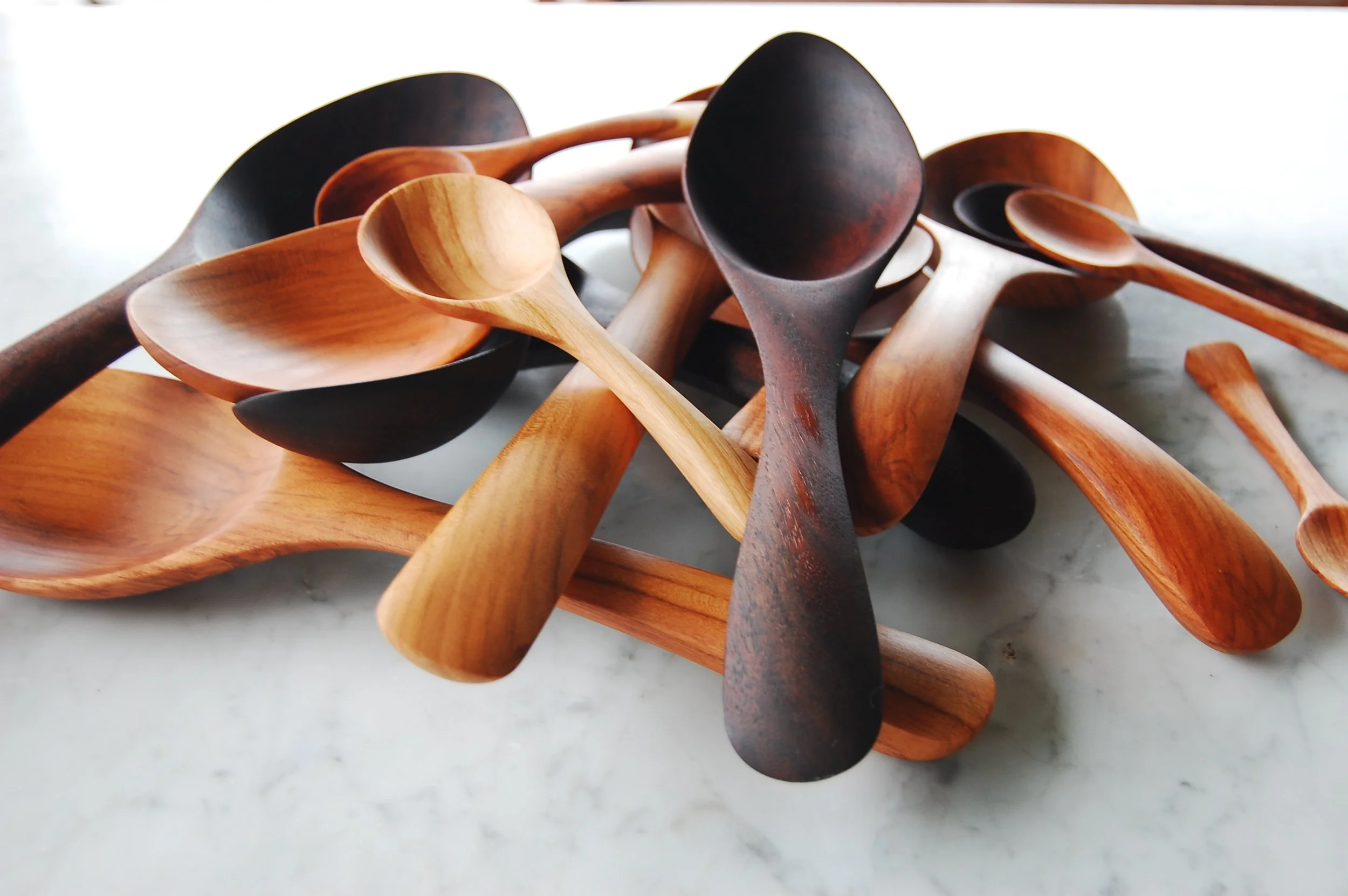 A pile of assorted wooden spoons and scoops, some dark-stained and some light, scattered on a white surface.