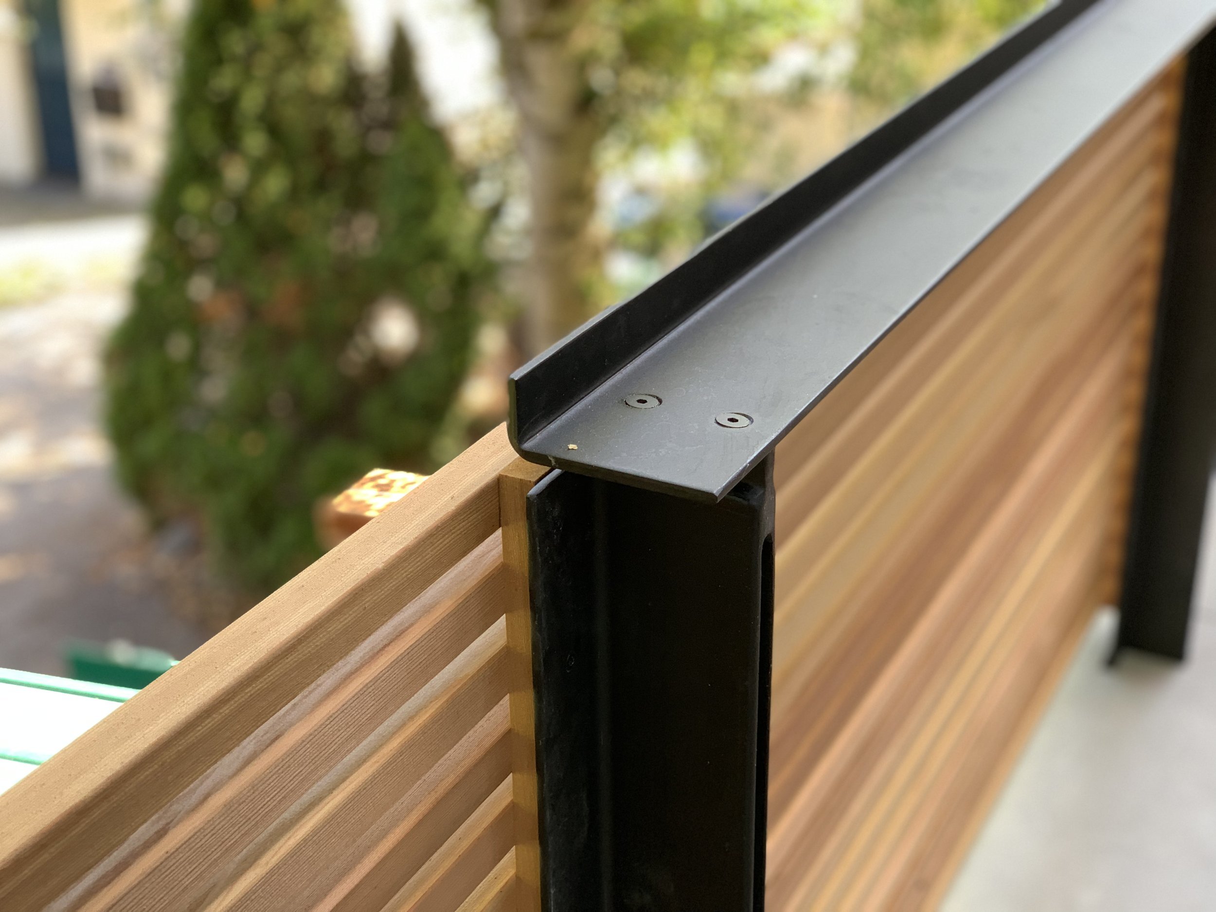 Close-up of a wooden and metal railing on a balcony, with trees and a sidewalk in the background.