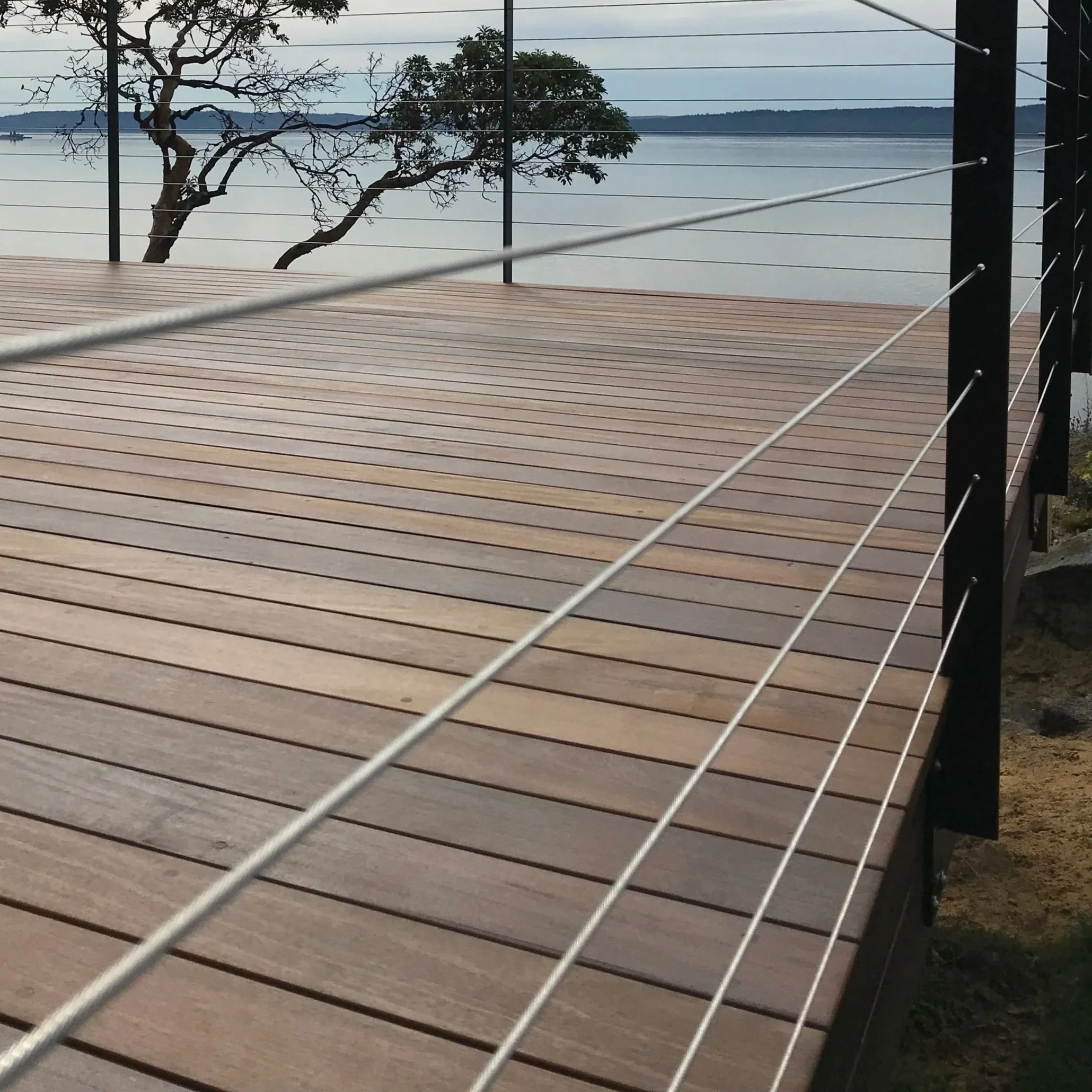 Wooden deck with cable railing overlooking a body of water and trees in the distance.