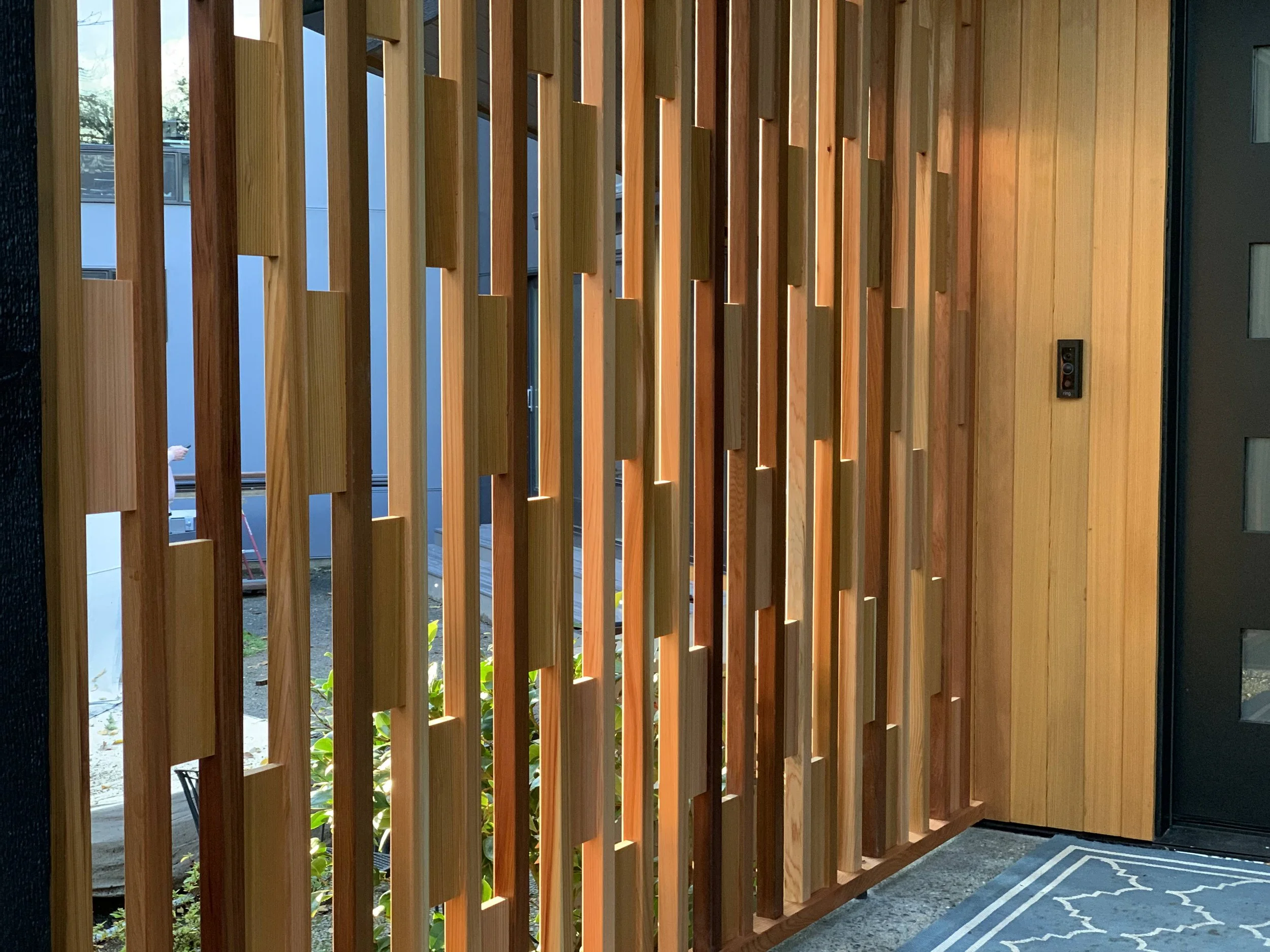 Interior view with custom wooden privacy screen and architectural feature with slats and paneling, door, and mat near entrance.