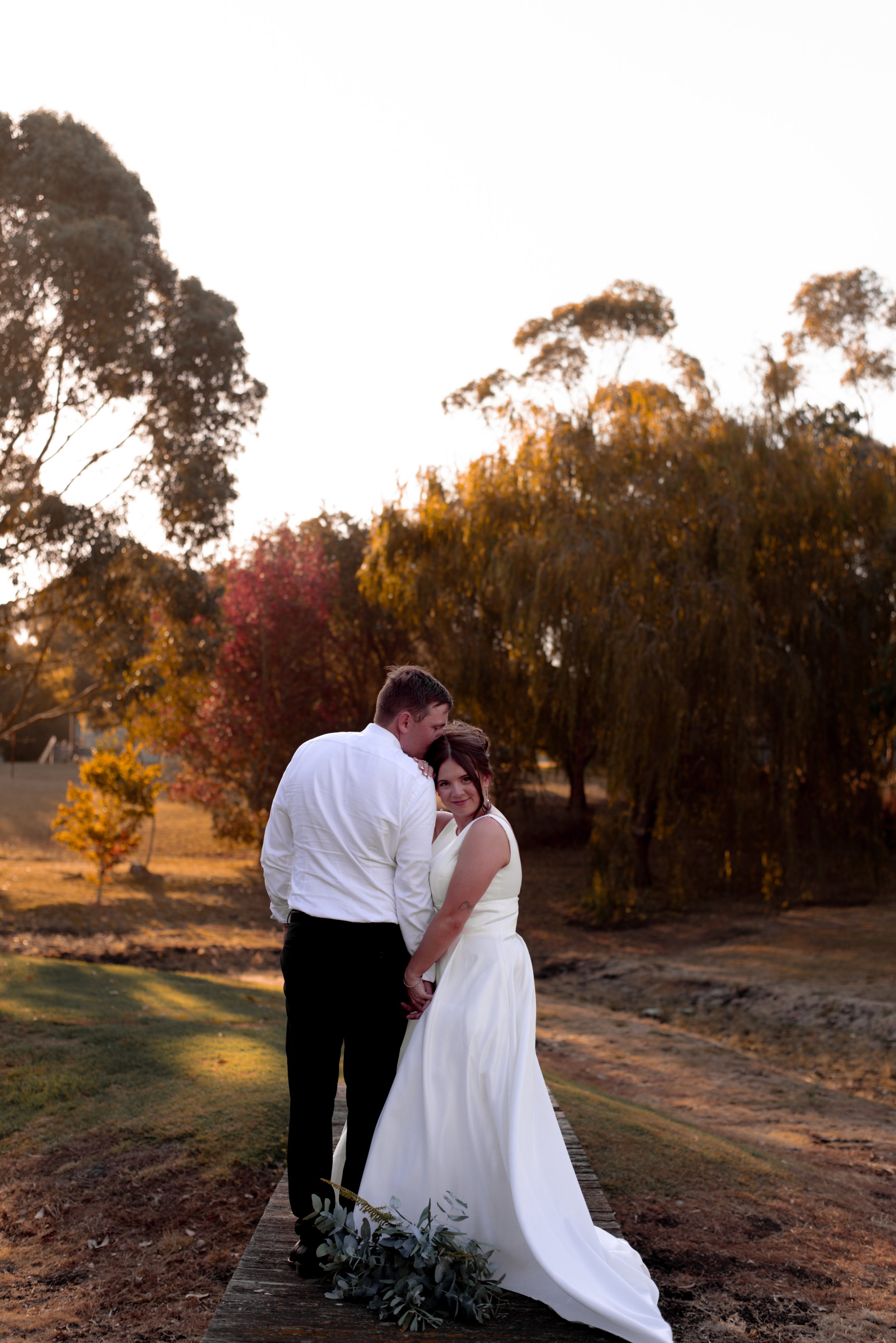 groom kissing bride on the forehead while embracing golden hour sunset