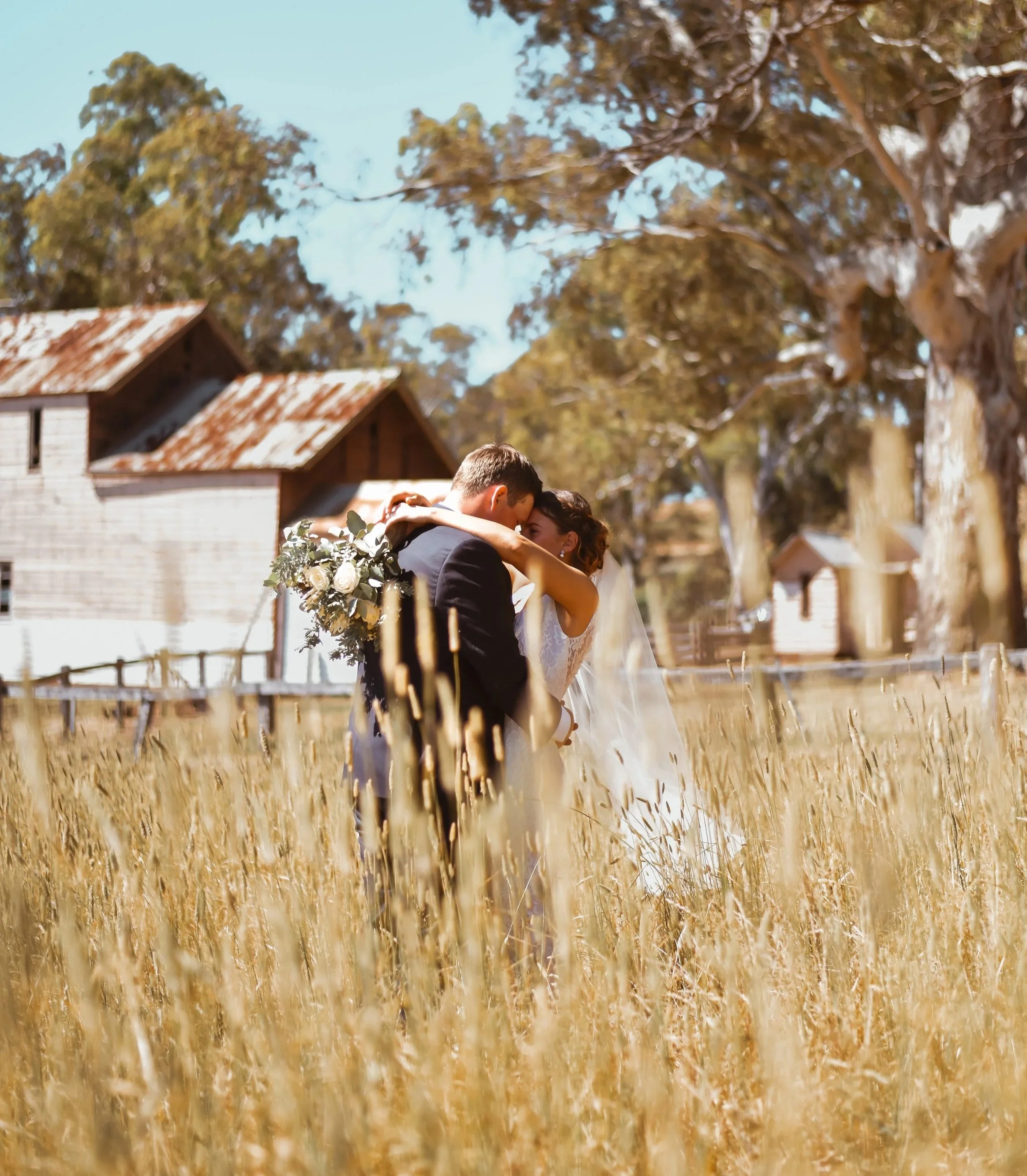 couple together in a paddock with long grass and a barn behind them