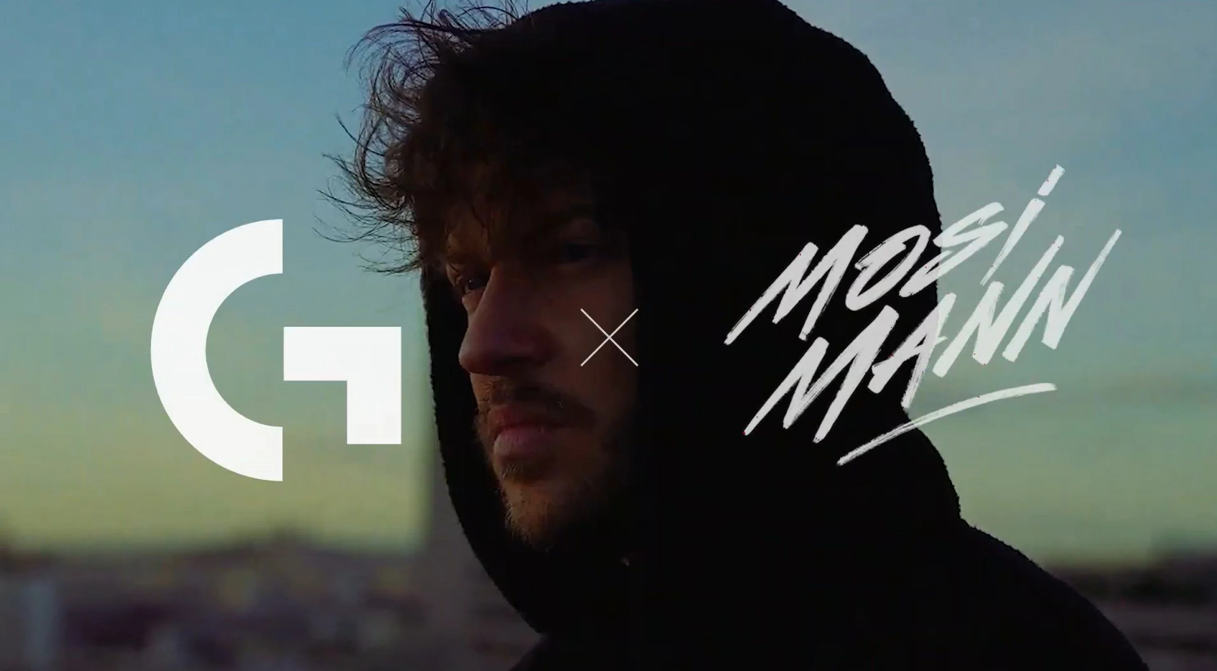Close-up of a man with messy hair wearing a black hoodie, standing outdoors during a sunset or sunrise, with stylized text overlay that says 'More Männ' and a logo on the left side.