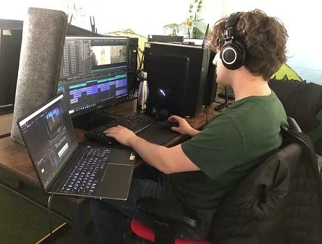 Person wearing headphones working on multiple monitors and a laptop at a desk.