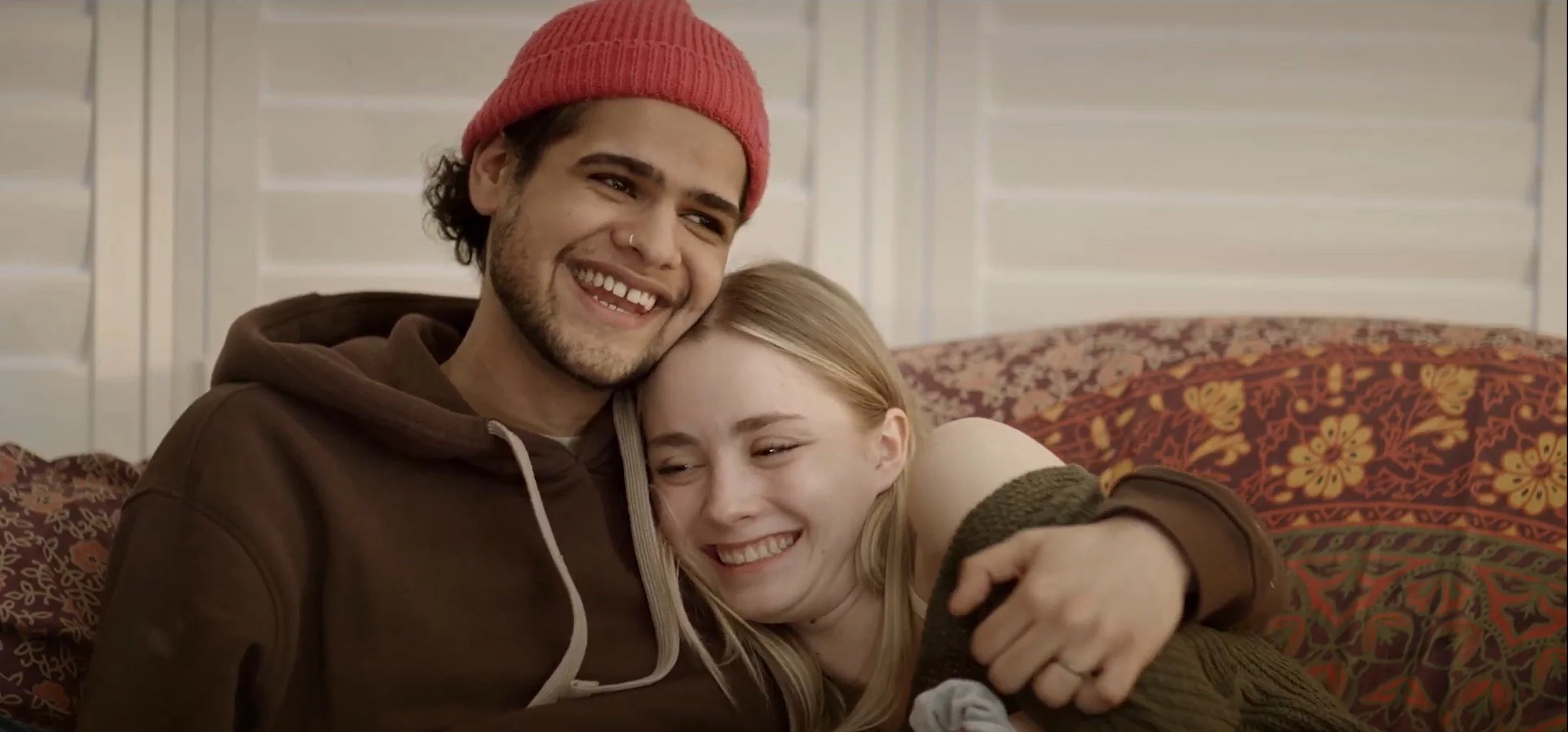 A young man and woman hugging and smiling happily on a sofa.