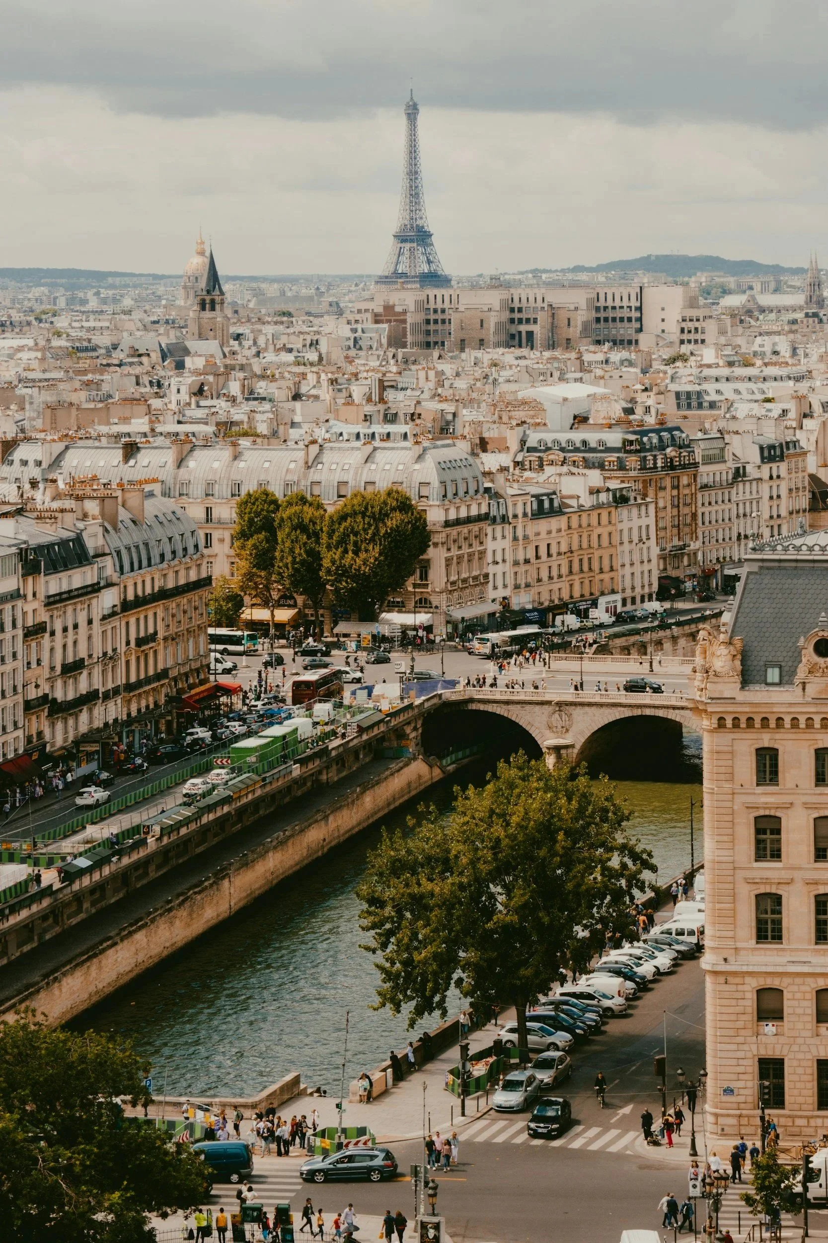 Vista urbana de París con la Torre Eiffel en el fondo, vista del río Sena y calles con tráfico y peatones.