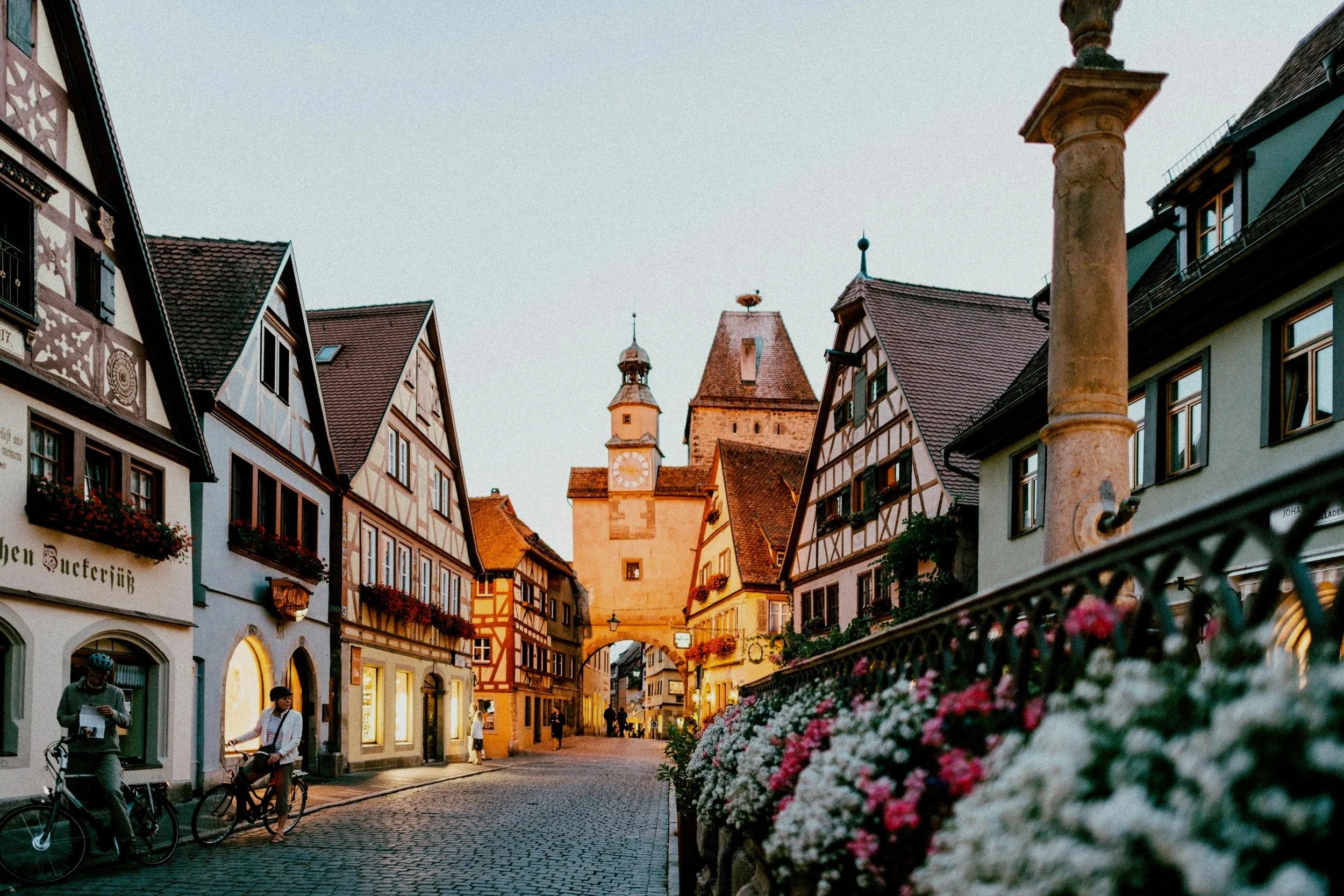 Calles históricas adornadas con casas de arquitectura tradicional alemana, una torre con reloj en el fondo, y personas paseando y en bicicleta.