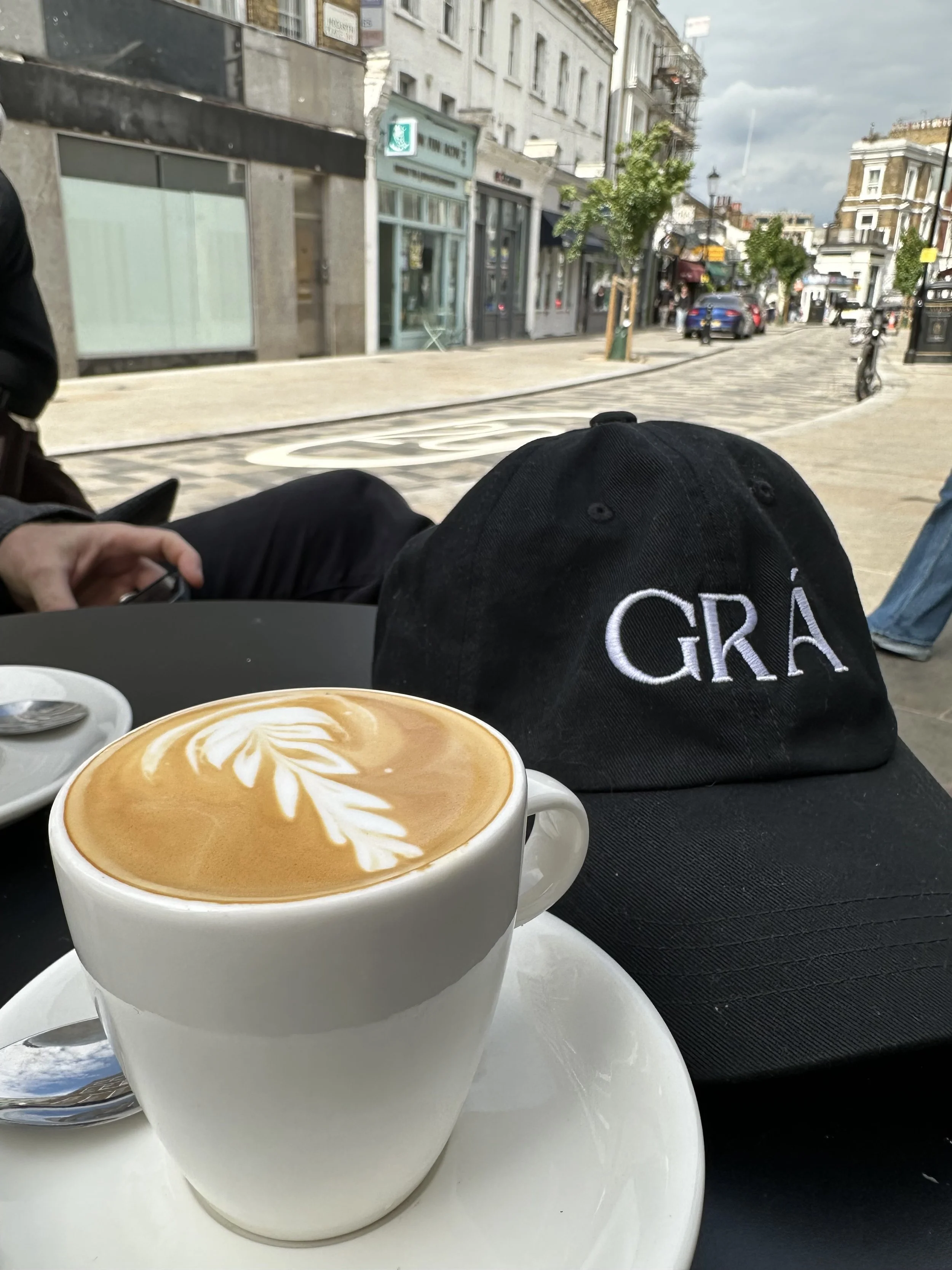 A white cup of latte with latte art on a table outside a café in Knightsbridge, London, with buildings and street scenery in the background.