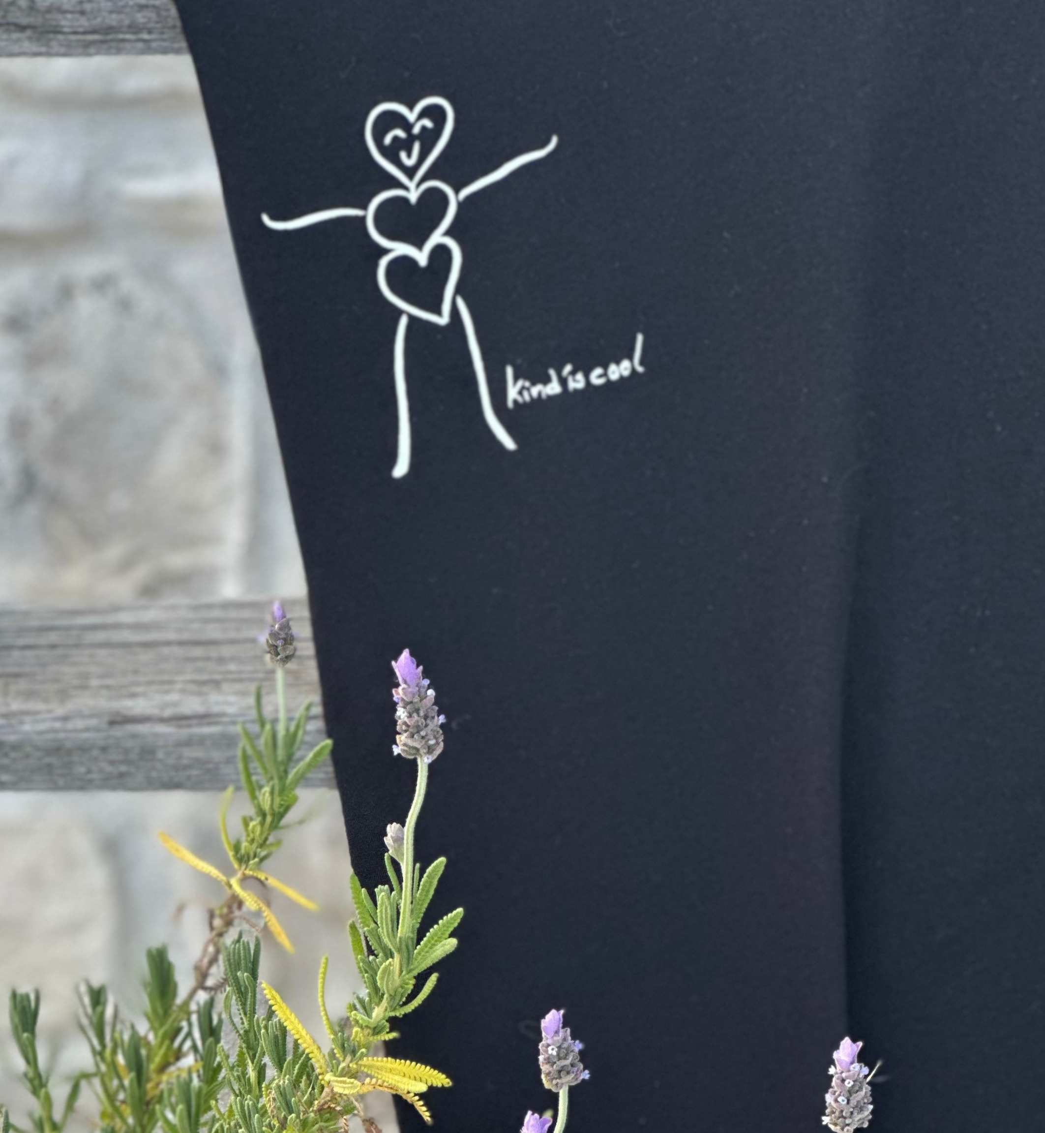Drawing of a person with three hearts stacked vertically as the body, with a smiling face and outstretched arms, accompanied by the phrase 'kind is cool' on a black background.