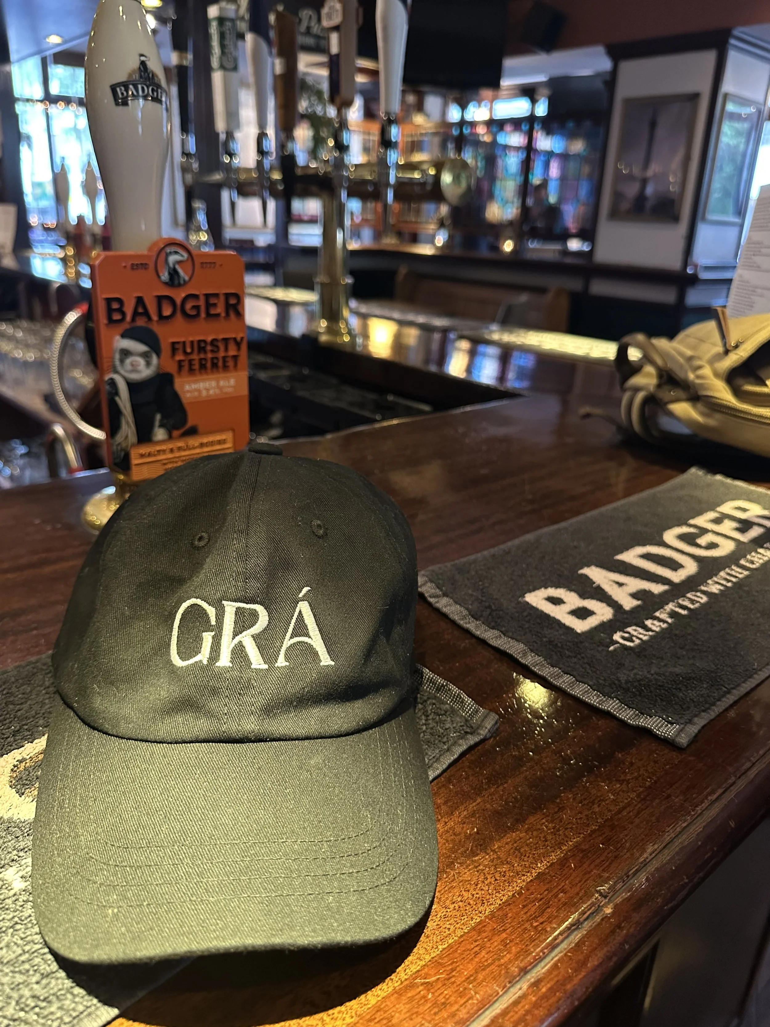 A black baseball cap featuring the word 'GRÁ on the front. It is the Irish word for LOVE. The cap sits on a pub bar in London near Paddington Station, London, England.