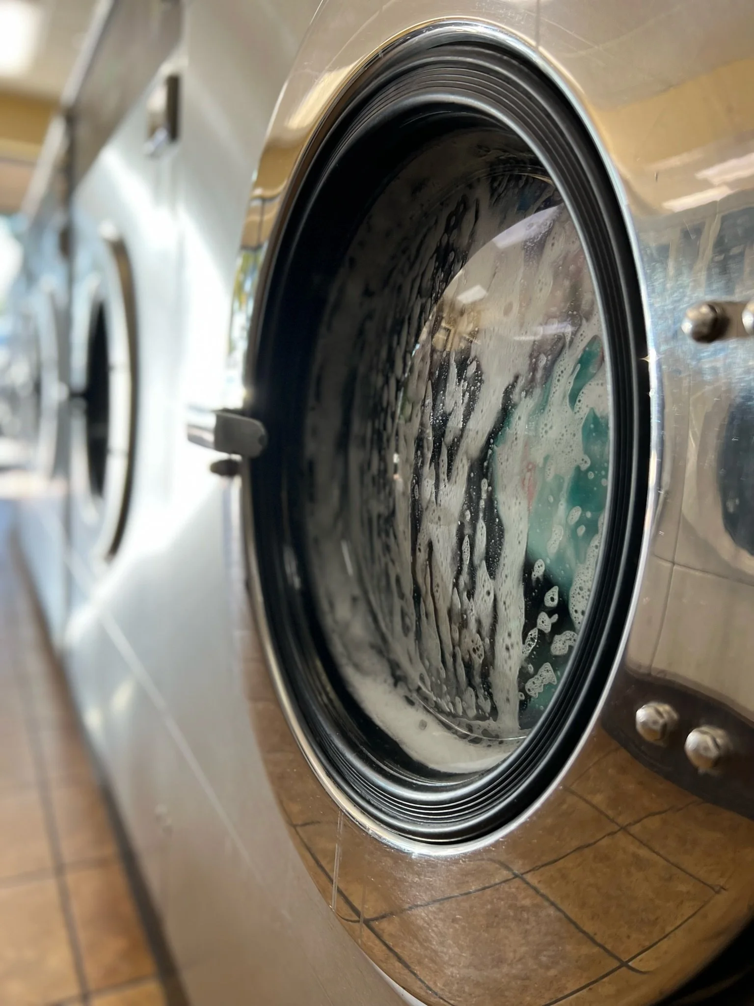 Washing machine with soapy water inside, partially open door, in a laundromat.
