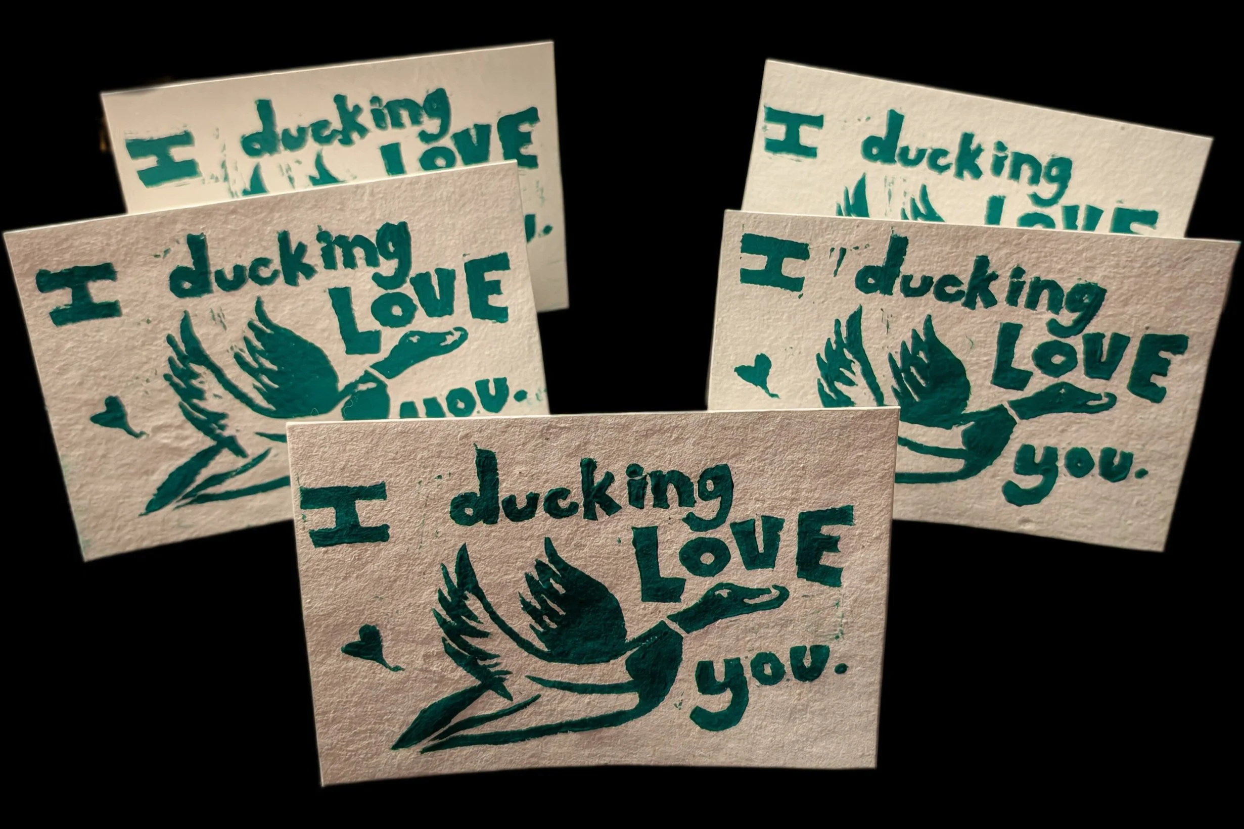 Group of four paper cards with a blue duck illustration and the phrase "I ducking love you" on a black background created for The Queen Inn, by Bronwyn Putman at Forgotten Loves