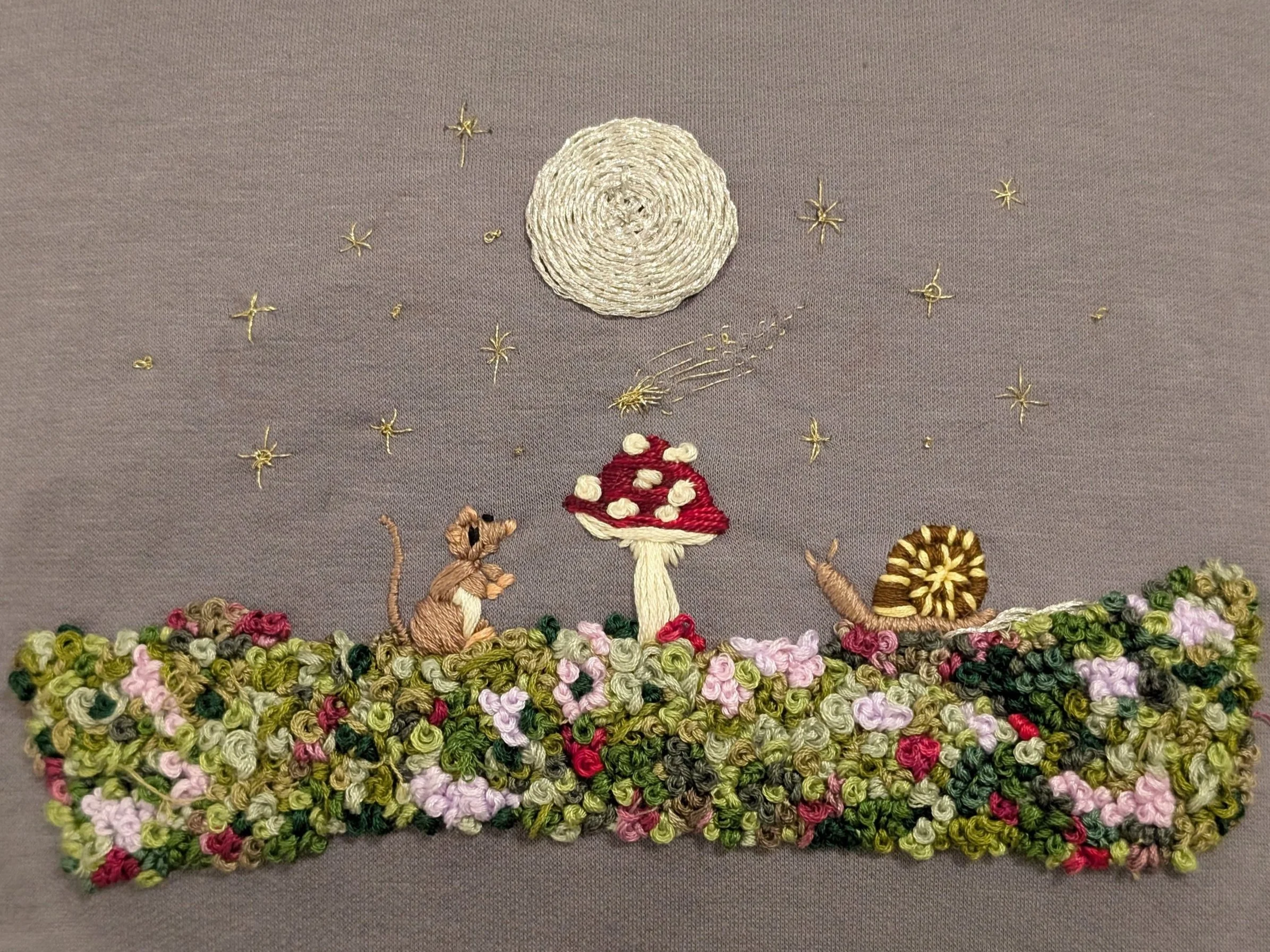 Bespoke embroidery of a whimsical scene with a moon, stars, a mouse, a mushroom, and a snail on a floral ground.
