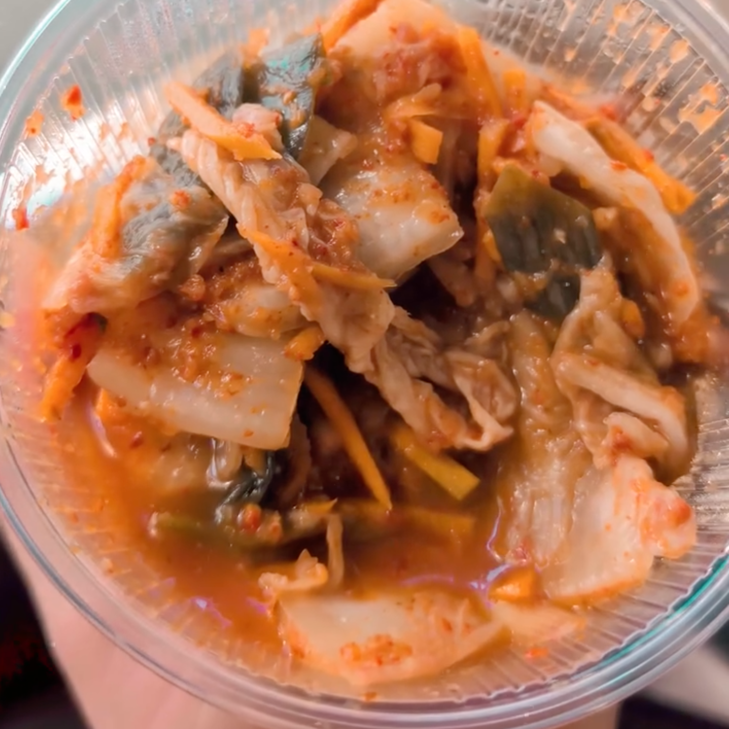 Close-up of kimchi, a traditional Korean fermented vegetable dish, in a clear plastic container, used in a social media post for The Crafty Pickle Co.