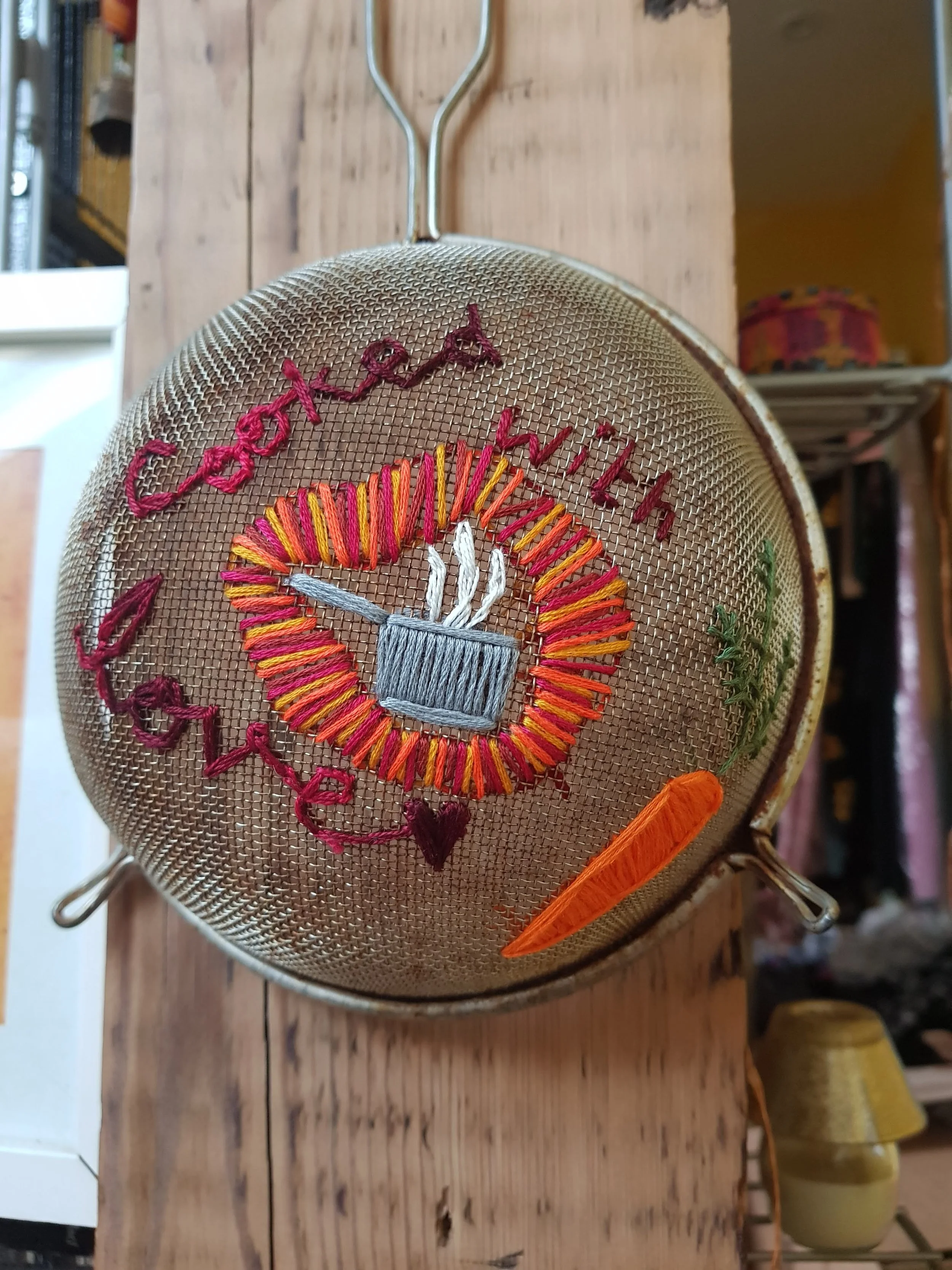 Bespoke embroidered sieve with the text 'Cooked with love' and illustrations, featuring vegetables.