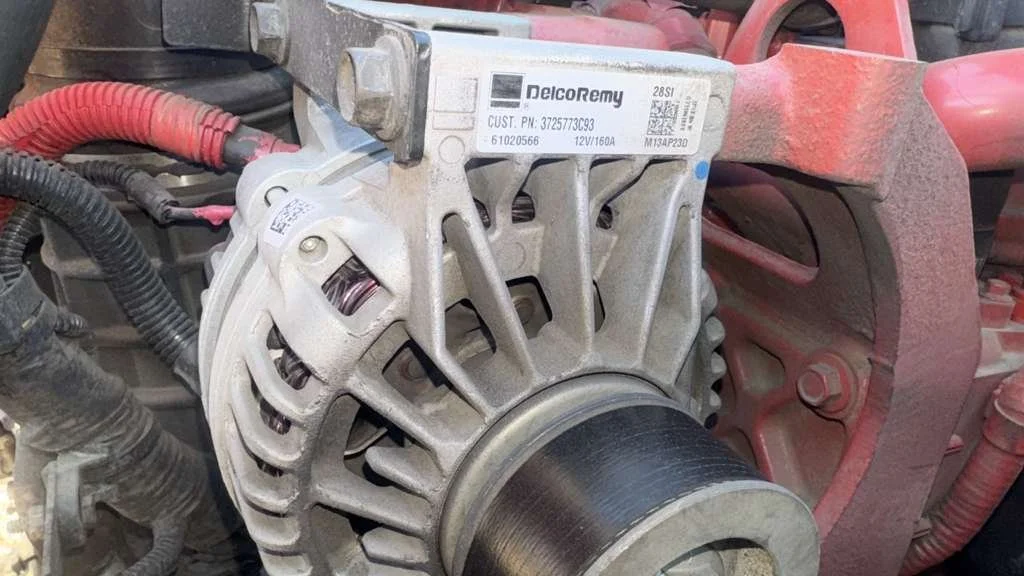 Close-up of an automotive alternator mounted on an engine, showing the pulley and electrical connections.