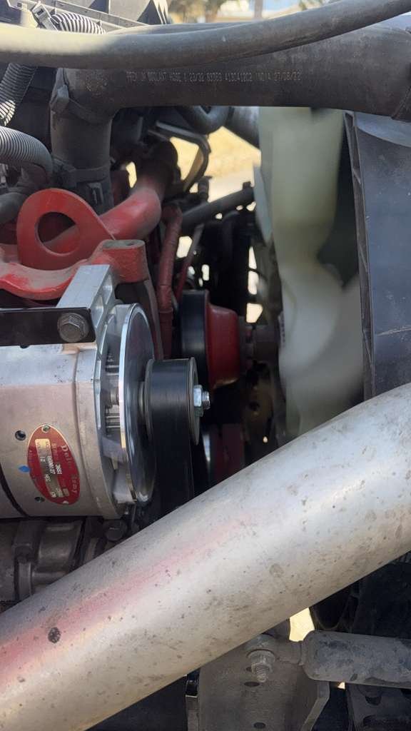 Close-up of a vehicle engine showing a belt-driven alternator, various hoses, and metal components.