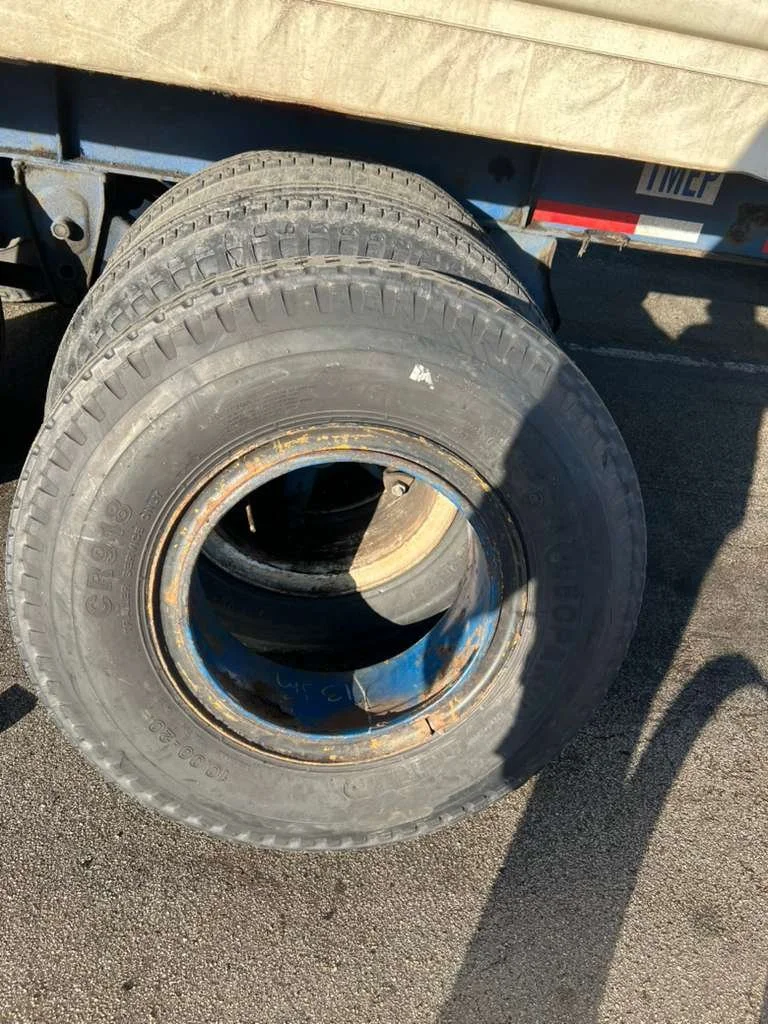 Close-up of four stacked tires with no rims, attached to a trailer or vehicle, on an asphalt surface with a rally of grime and dirt.