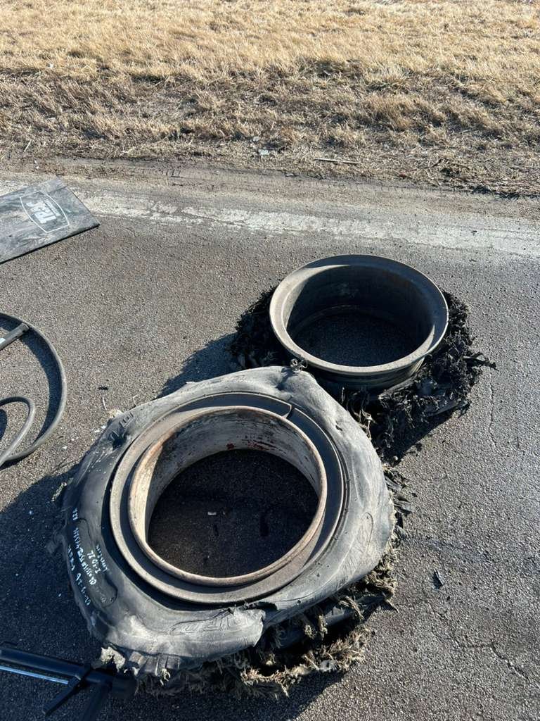Two large, used tires with no rims, sitting on a paved road near a grassy area, with some debris and a folded sign nearby.