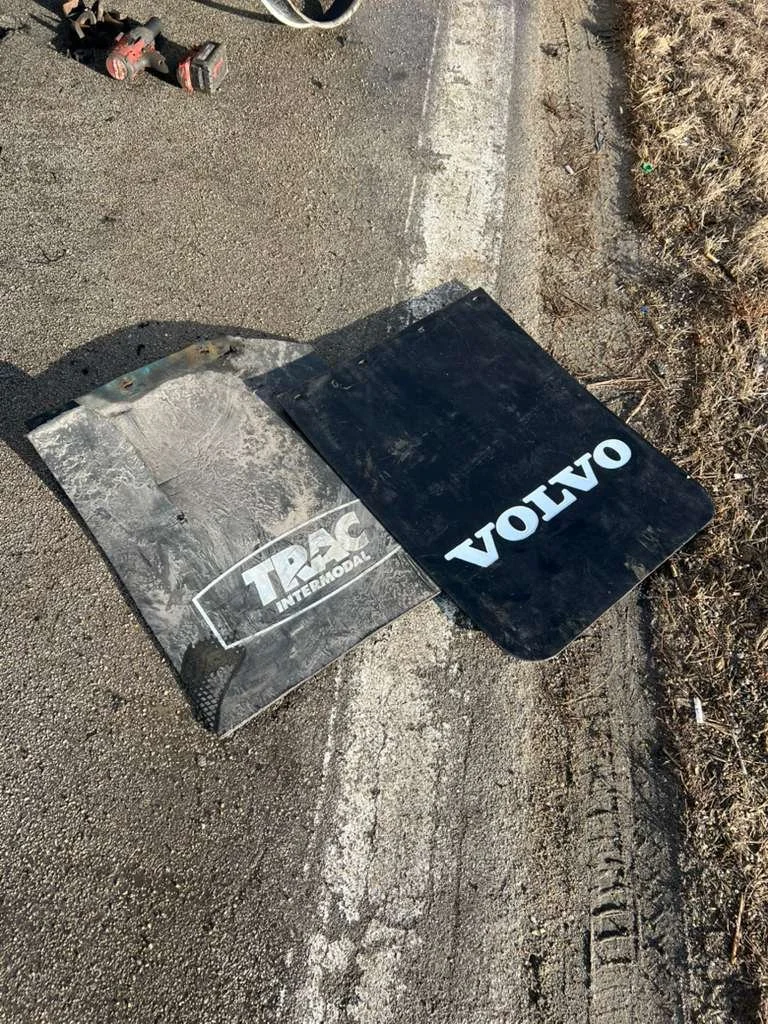 Two car mud flaps, one with the TRAC Intermodal logo and the other with the Volvo logo, lying on the side of a road.