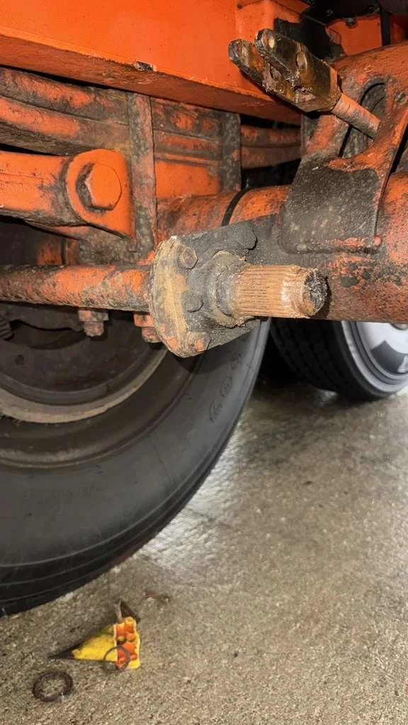 Close-up of a rusted tractor axle with a large black tire in a garage or workshop.