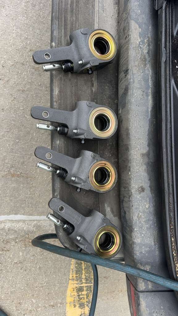 Four automotive brake calipers lying on a concrete surface next to a vehicle's wheel well.