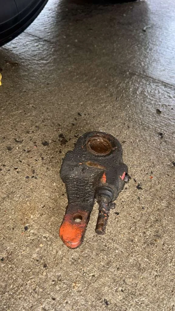 A heavily rusted and dirty universal joint with an orange-painted arm lying on a concrete floor.