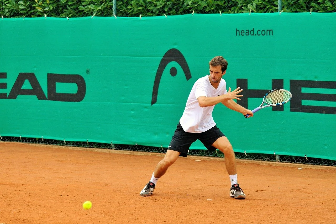 A man playing tennis on a clay court, preparing to hit a tennis ball with a racket.