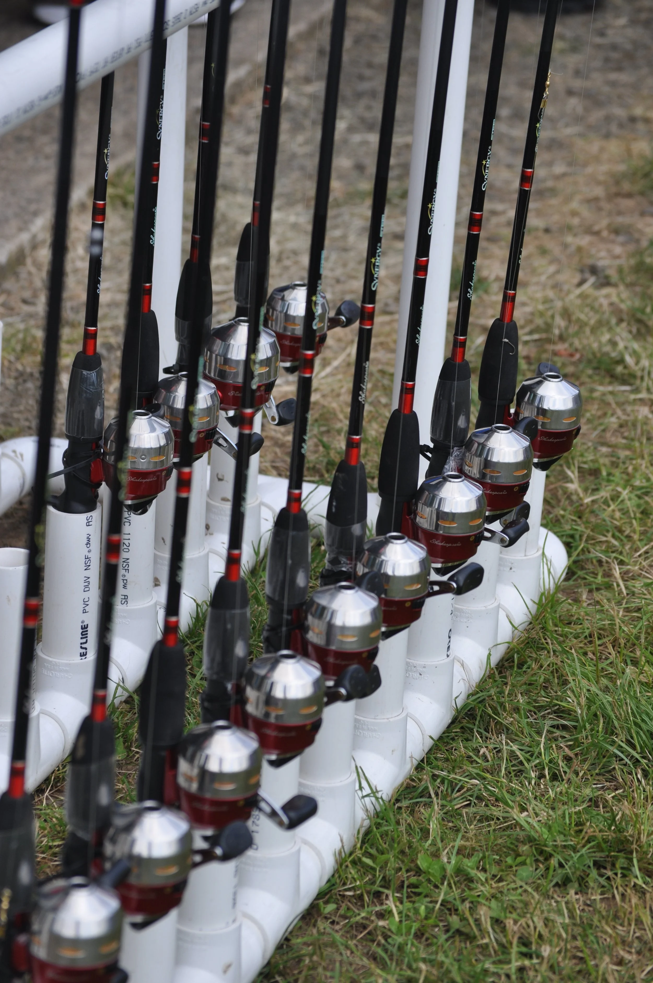 Multiple fishing rods with reels mounted in white PVC pipe holders on grass, ready for fishing.