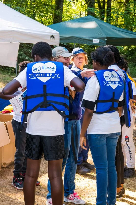 Group of young girls with life jackets in a wooded outdoor setting, likely at a boat safety event.