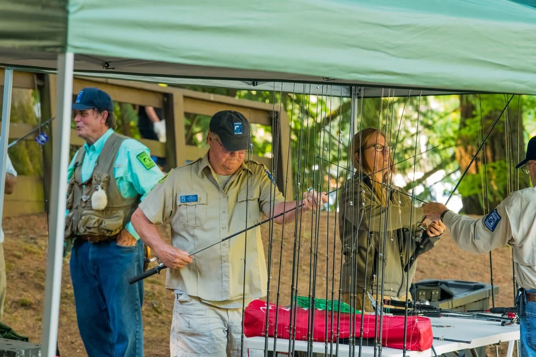 Four people, likely park rangers, participating in a fishing activity under a green canopy in a park, with trees in the background.