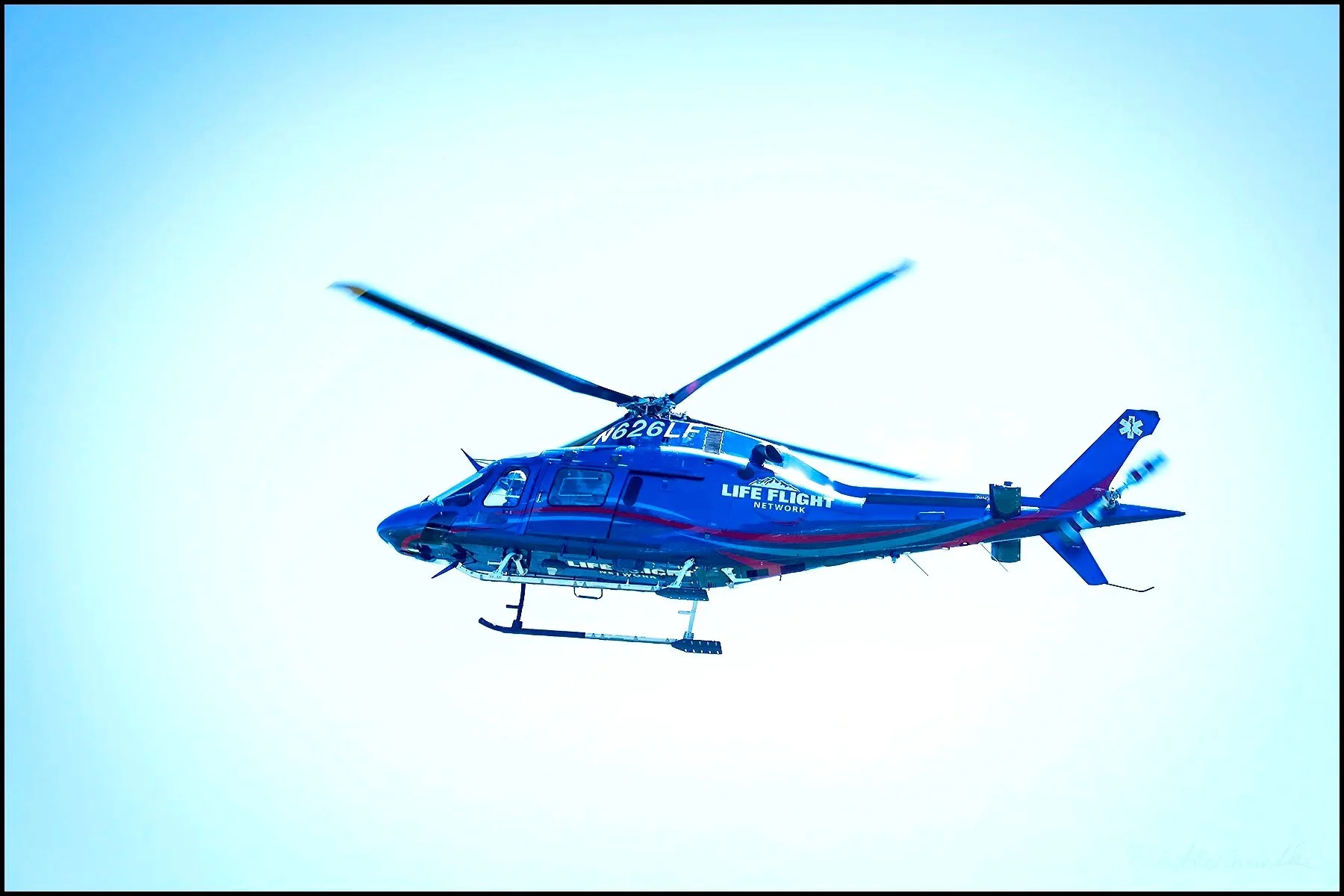 A blue helicopter marked with 'LIFE FLIGHT NETWORK' flying in a clear sky.