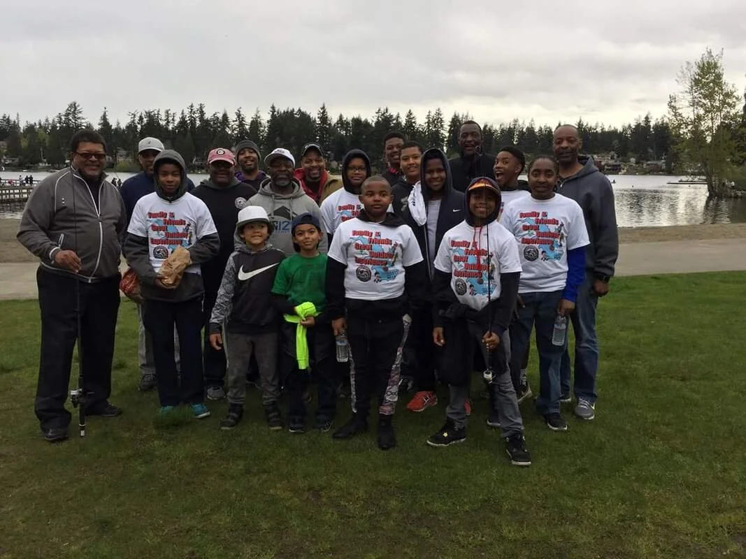 Group of children and adults posing outdoors near a lake on cloudy day