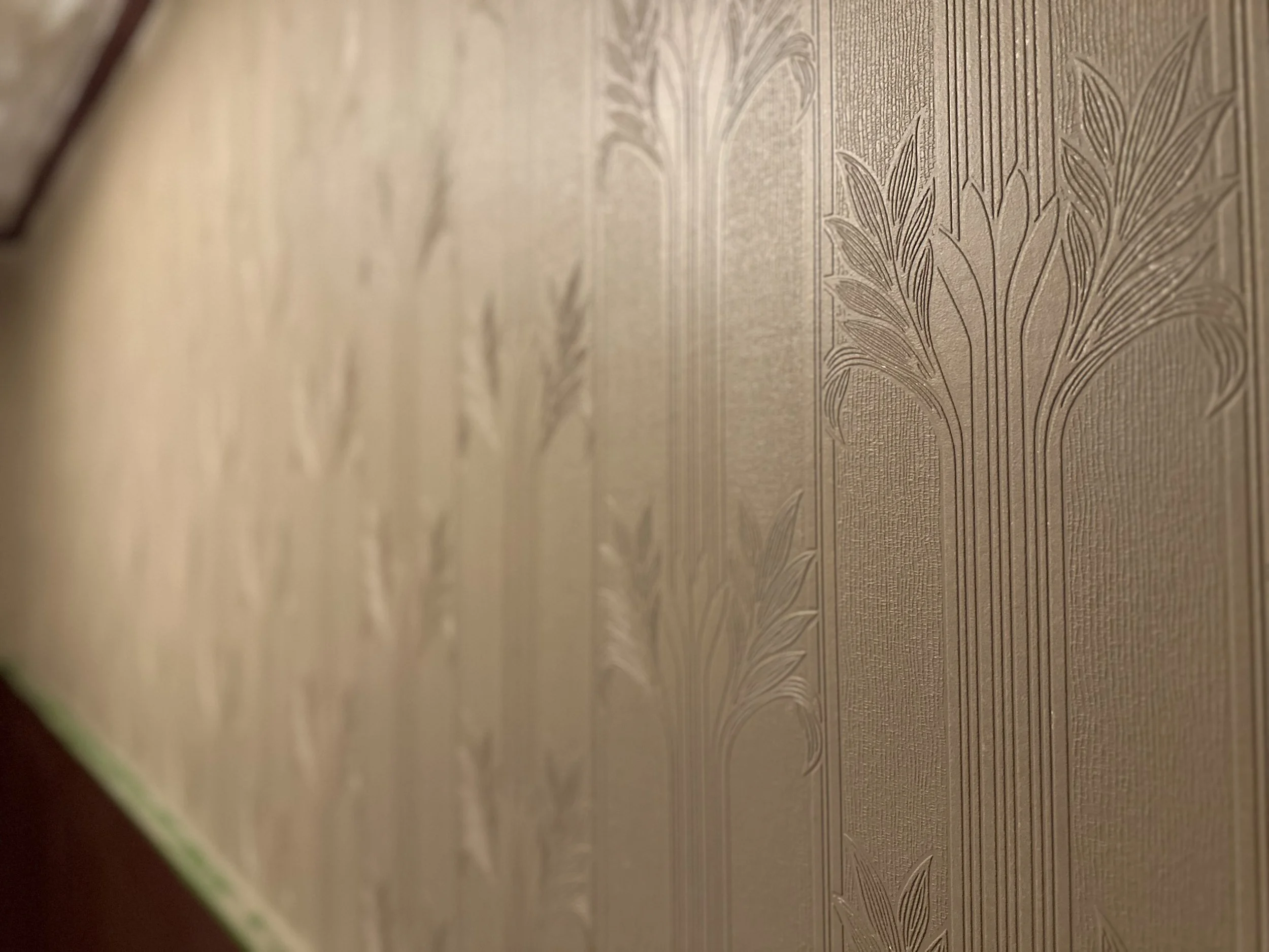 Close-up of textured wallpaper with vertical striped pattern and botanical leaf designs in beige and gold tones.