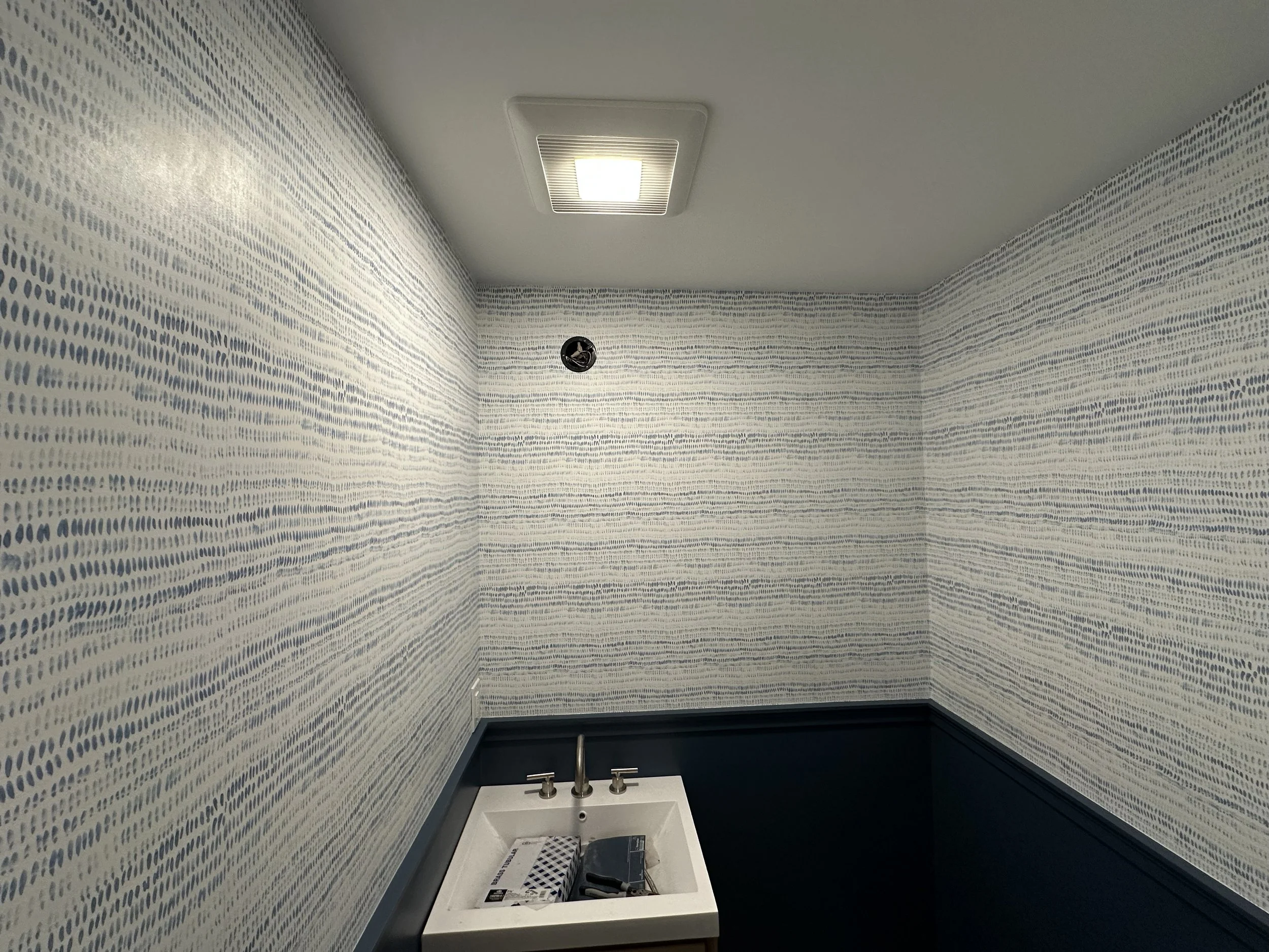 Small bathroom with patterned wallpaper, a white sink with a faucet, and a ceiling vent.