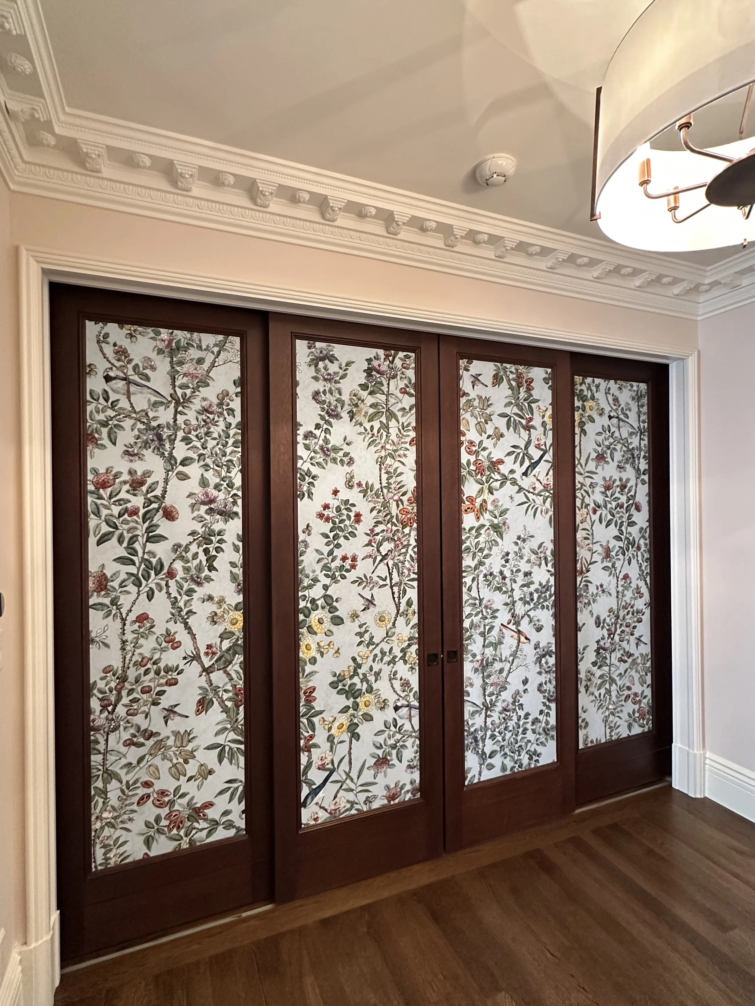 Room with wooden wardrobe featuring floral patterned sliding doors, crown molding, and hardwood floors.