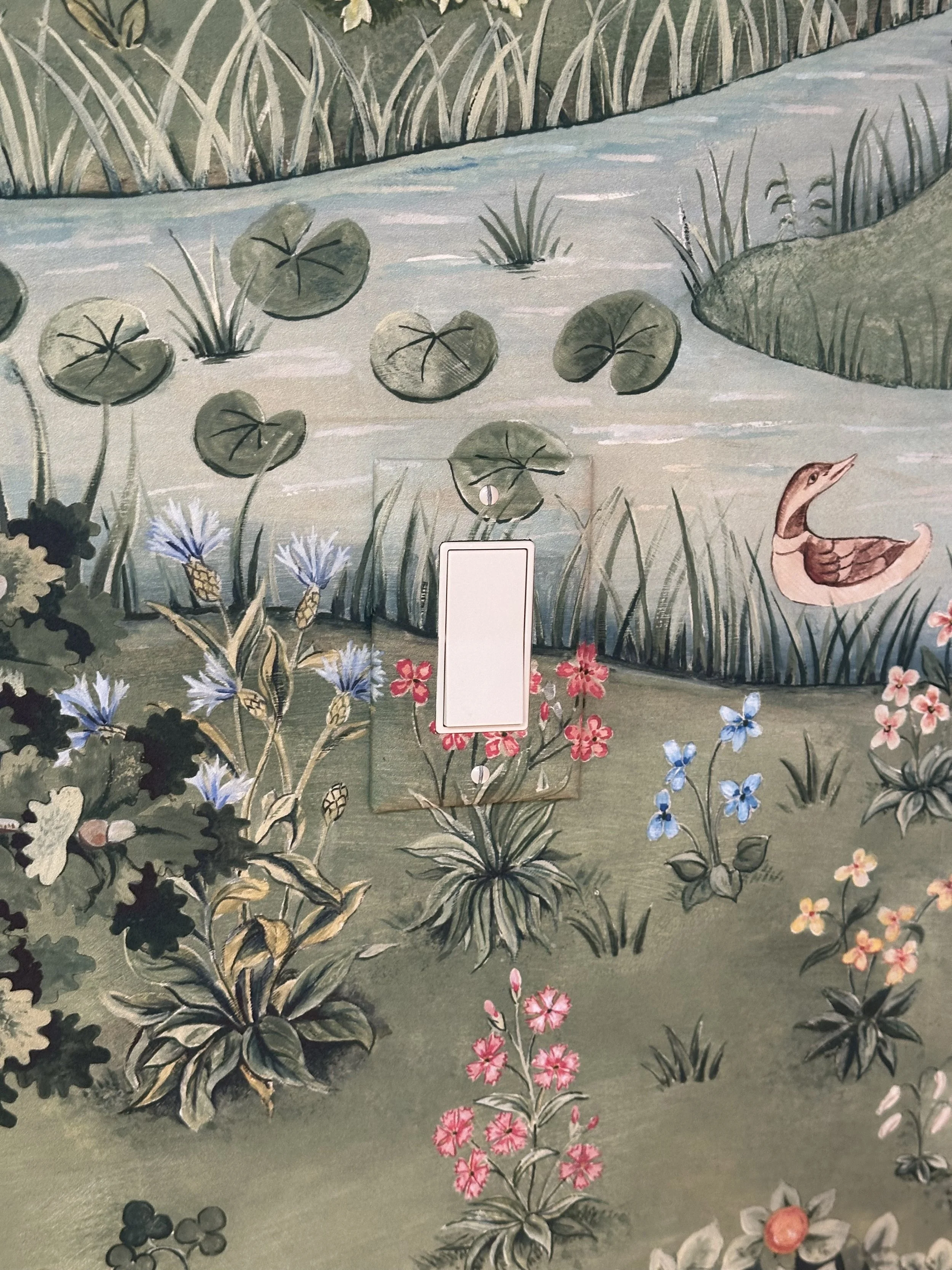 A mural of a pond scene with lily pads, aquatic plants, colorful flowers, a duck, and other lush greenery.