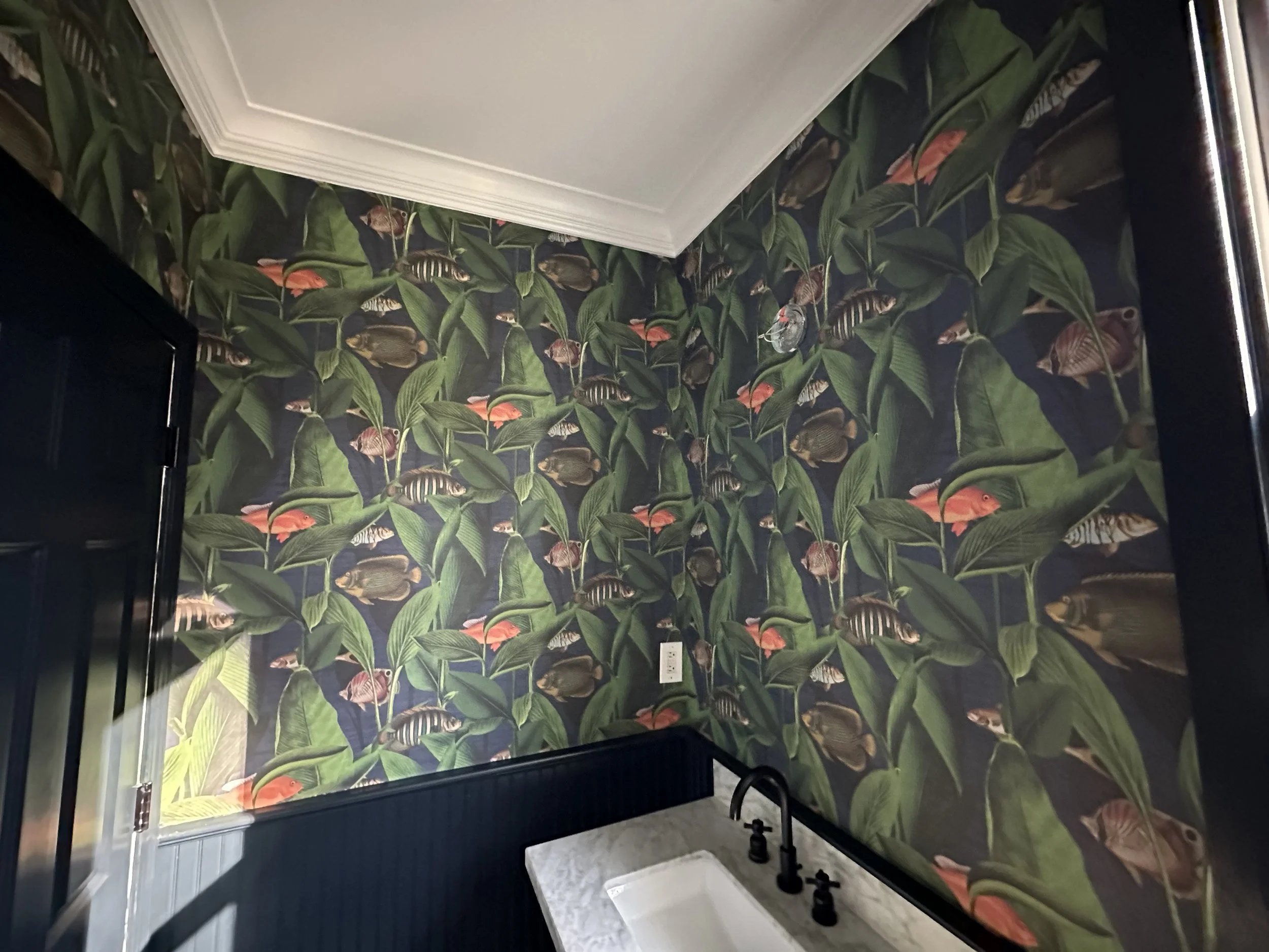 Bathroom with tropical fish and plant wallpaper, white ceiling, and a black faucet with a white sink